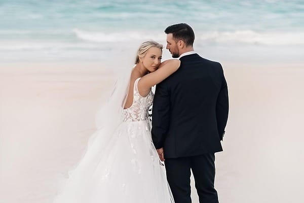 Bride and groom share a wedding embrace on the beach at Secrets Maroma, waves in the background.