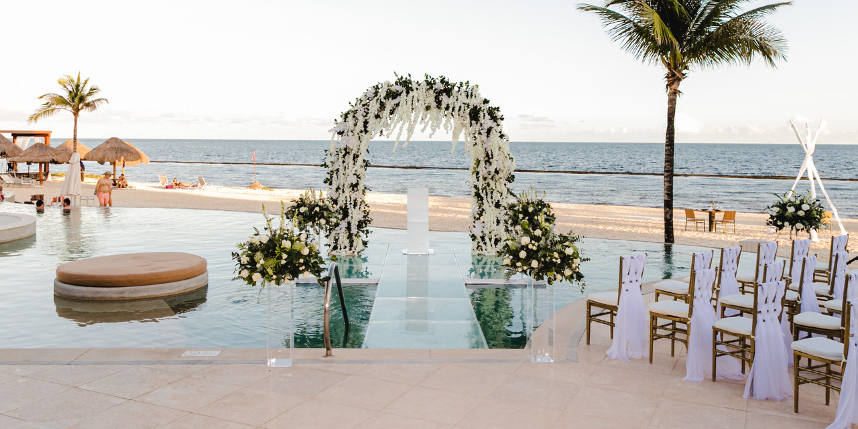 Destination wedding arch with white flowers by a pool at Secrets Riviera Cancun, overlooking the ocean.