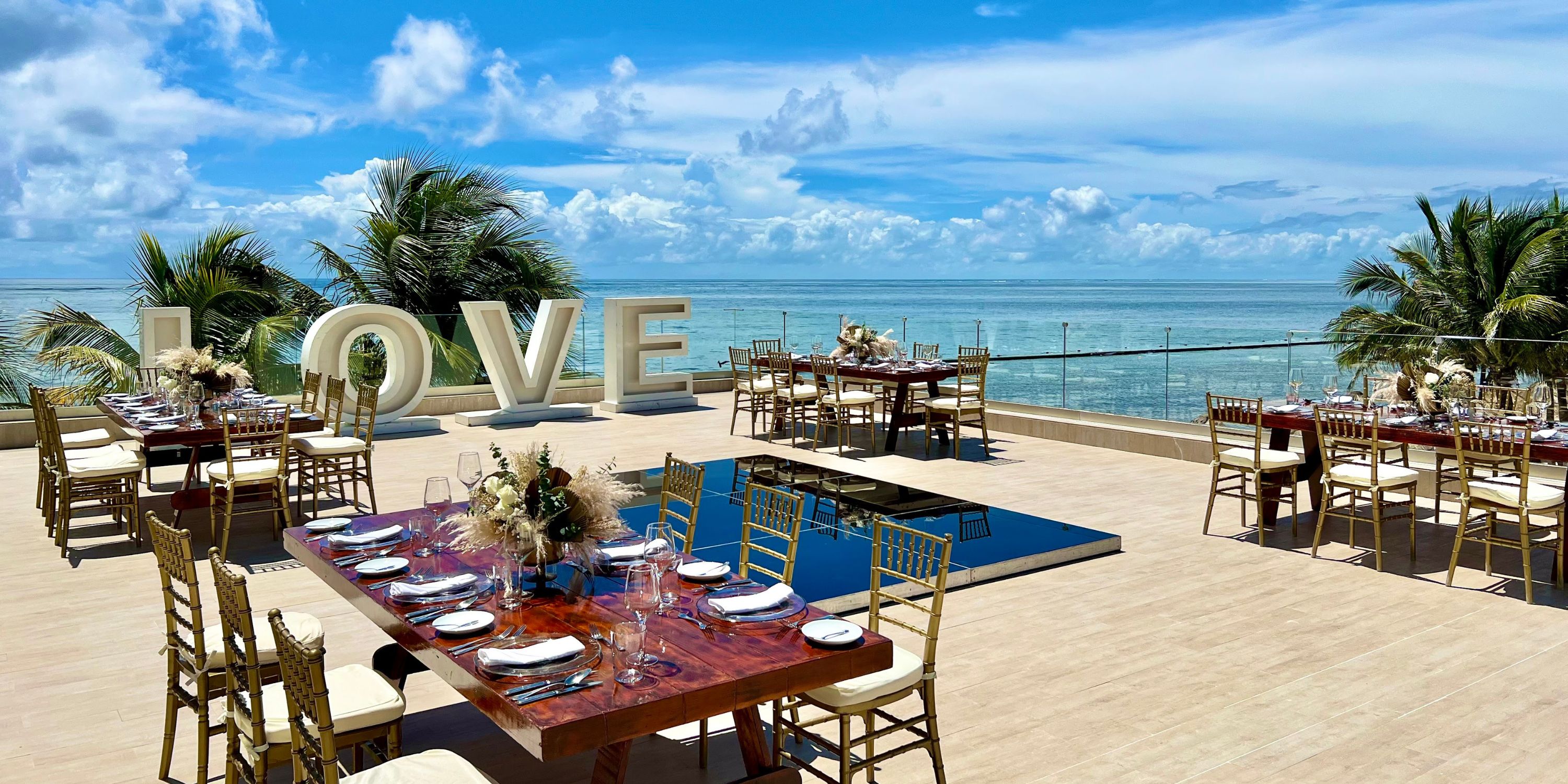 Destination wedding on Secrets Riviera Cancun terrace with LOVE sign, ocean view, and decorated tables.