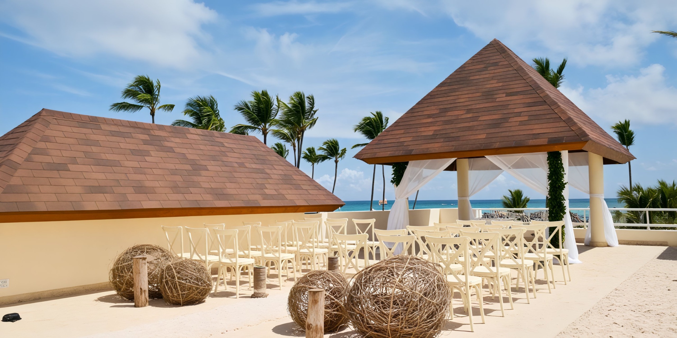 Destination wedding setup featuring wooden chairs and elegant decorative spheres, all set against a stunning ocean view under a clear sky.