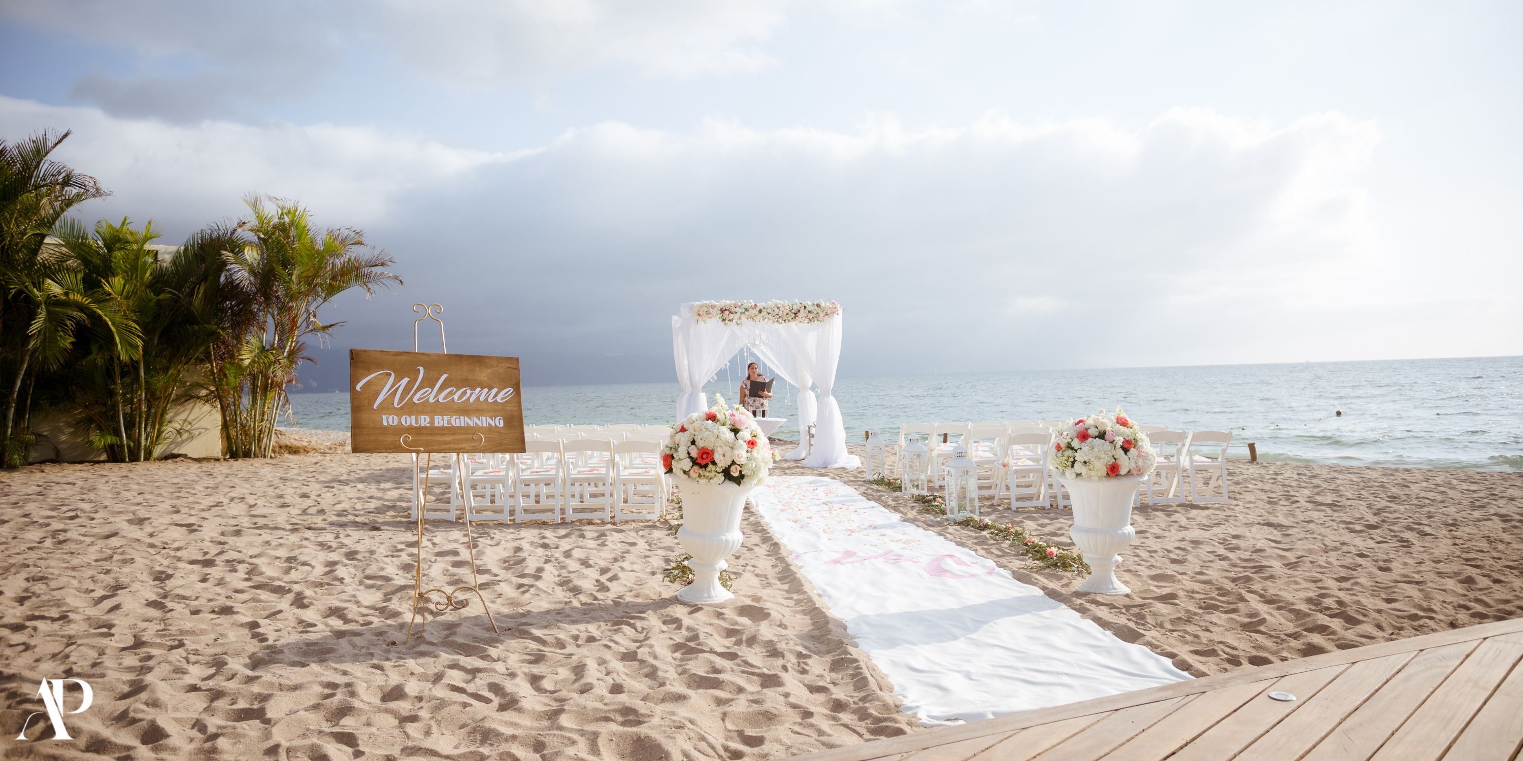 Destination wedding setup at Secrets Vallarta Bay with chairs, florals, and a &ldquo;Welcome&rdquo; sign by the sea.