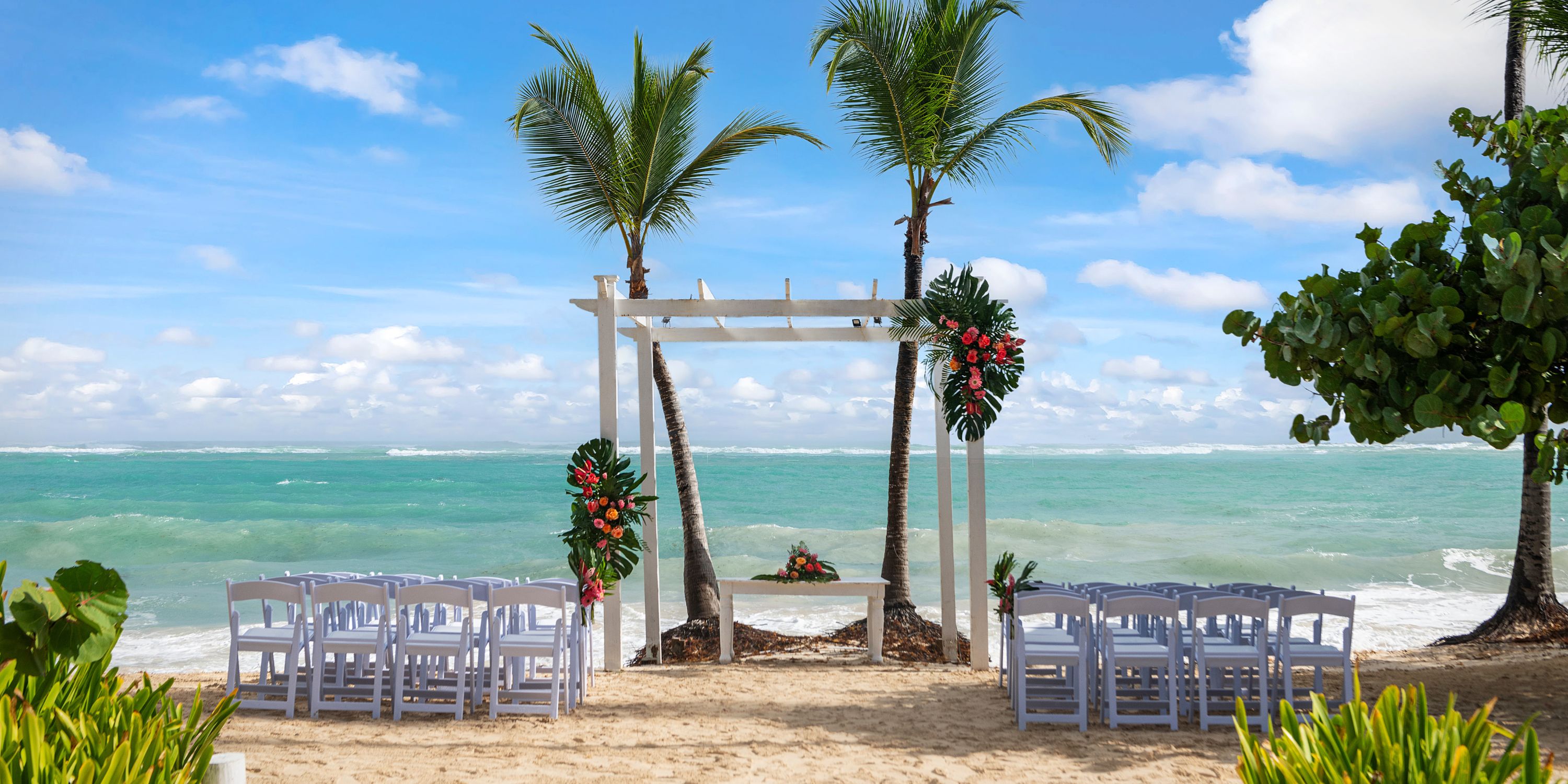 White chairs and an arch await a destination wedding at TRS Turquesa, beneath swaying palm trees.