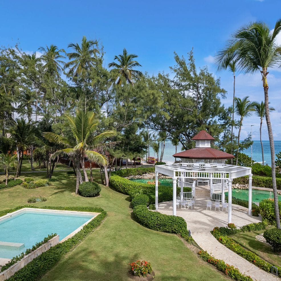 A white gazebo and square pool on a manicured lawn with palm trees, perfect for a destination wedding.