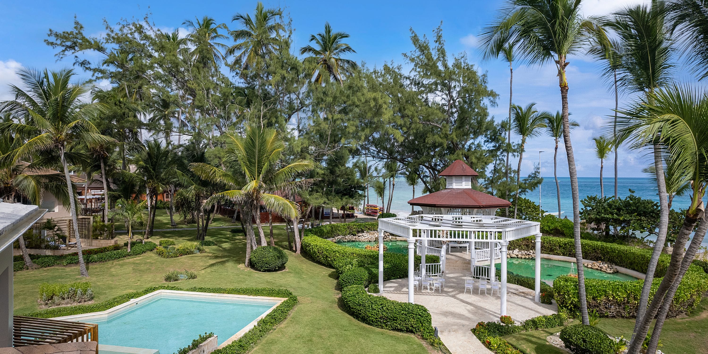 TRS Turquesa: White gazebo and two pools with palm trees by the ocean, ideal for a destination wedding.