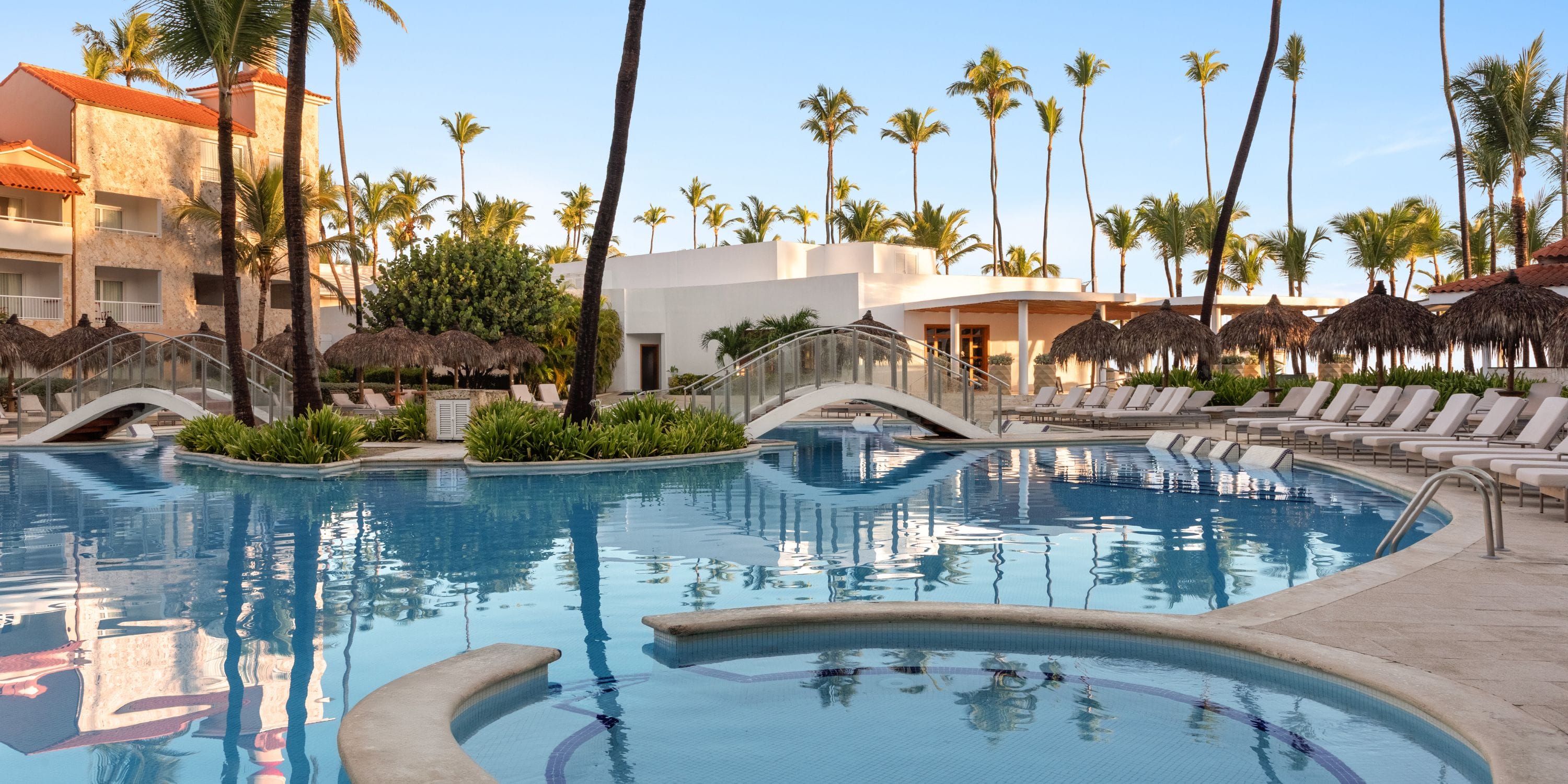 TRS Turquesa outdoor pool, ideal for a destination wedding, with lounge chairs, palms, and arched bridges.