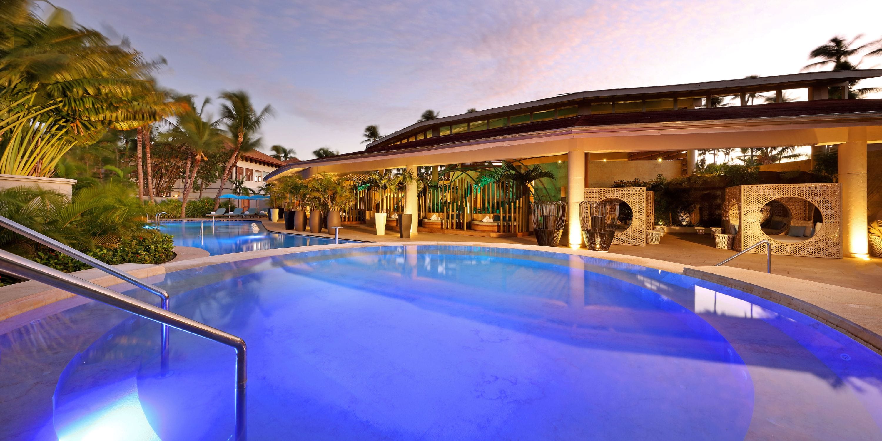 TRS Turquesa outdoor pool with blue lights, perfect for a destination wedding, beside palms at dusk.