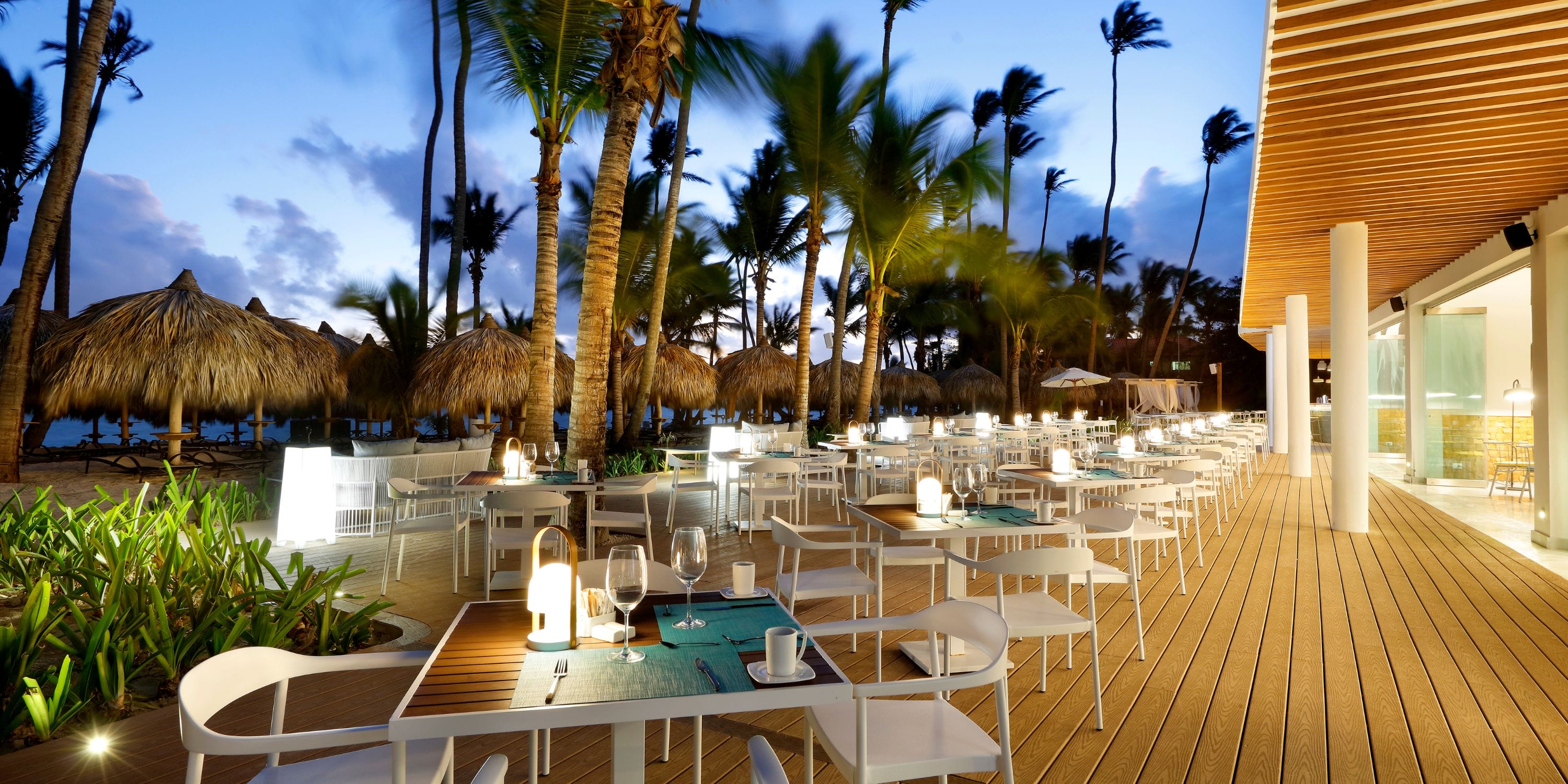 TRS Turquesa restaurant set for a destination wedding, with palm trees and thatched umbrellas at dusk.