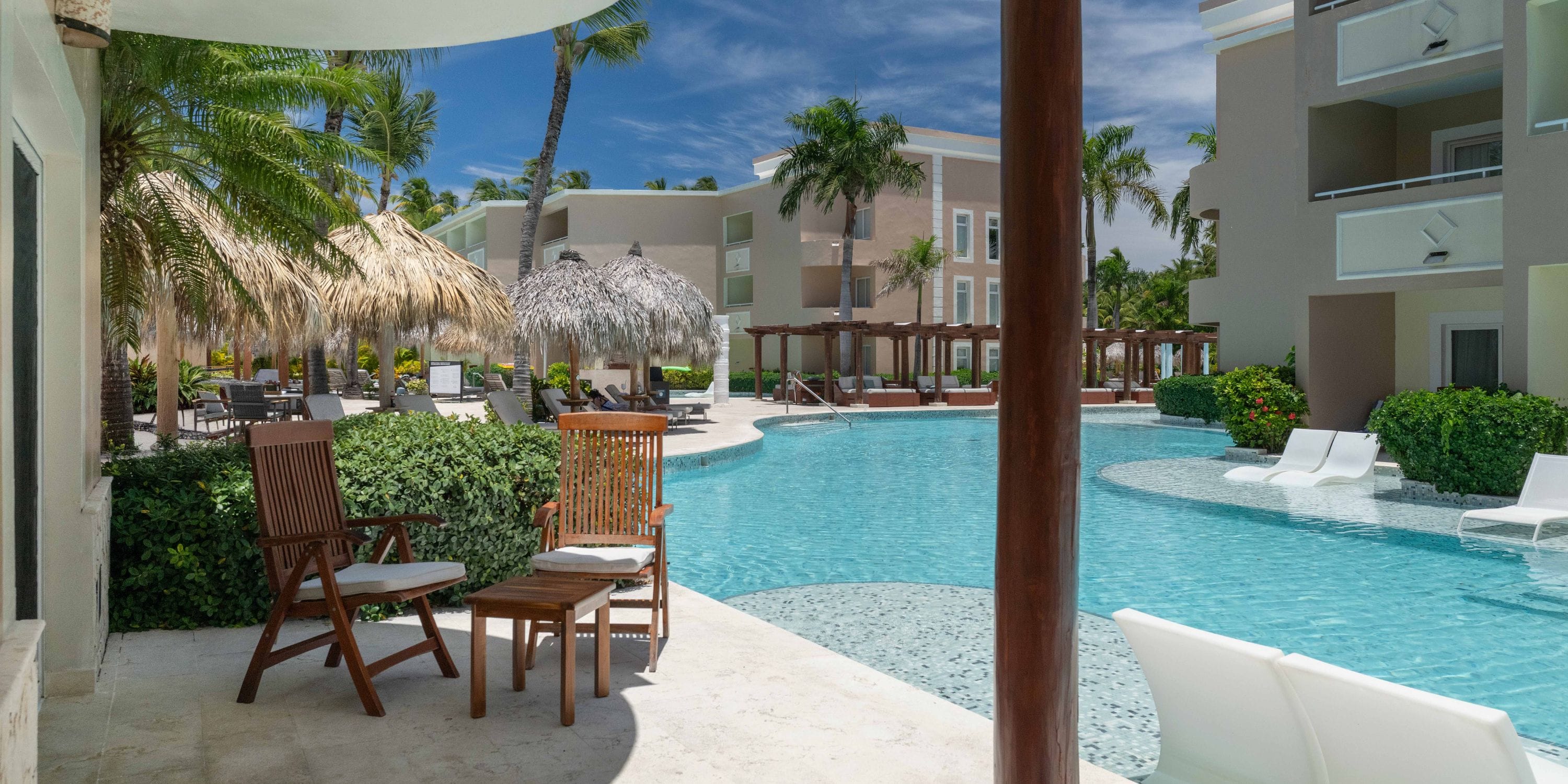 TRS Turquesa's pool area, ideal for a destination wedding, offers lounge chairs and palm trees under clear skies.