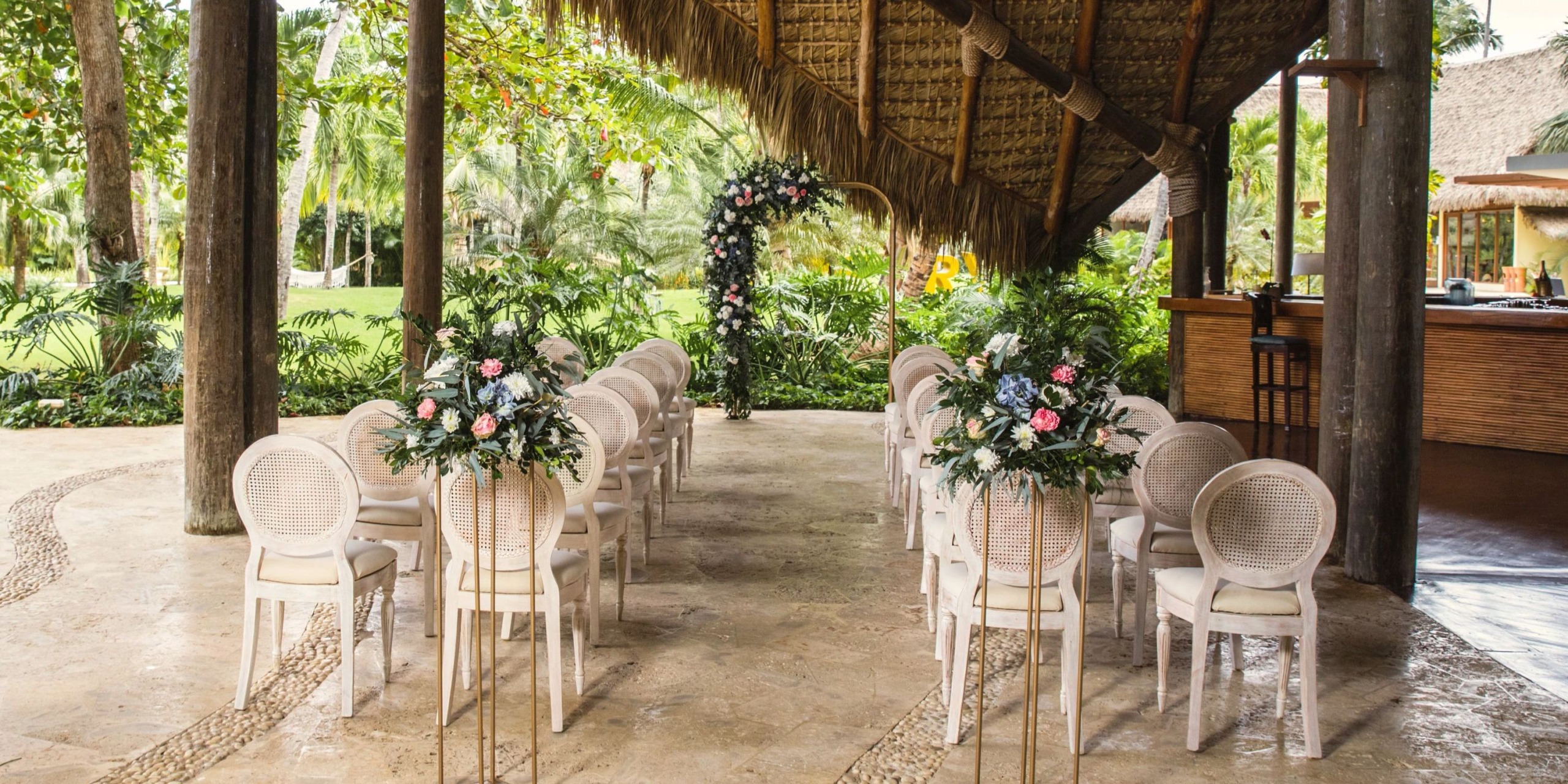 Zoetry Agua Punta Cana features an enchanting outdoor destination wedding setup, complete with elegant chairs and a beautifully adorned floral arch.