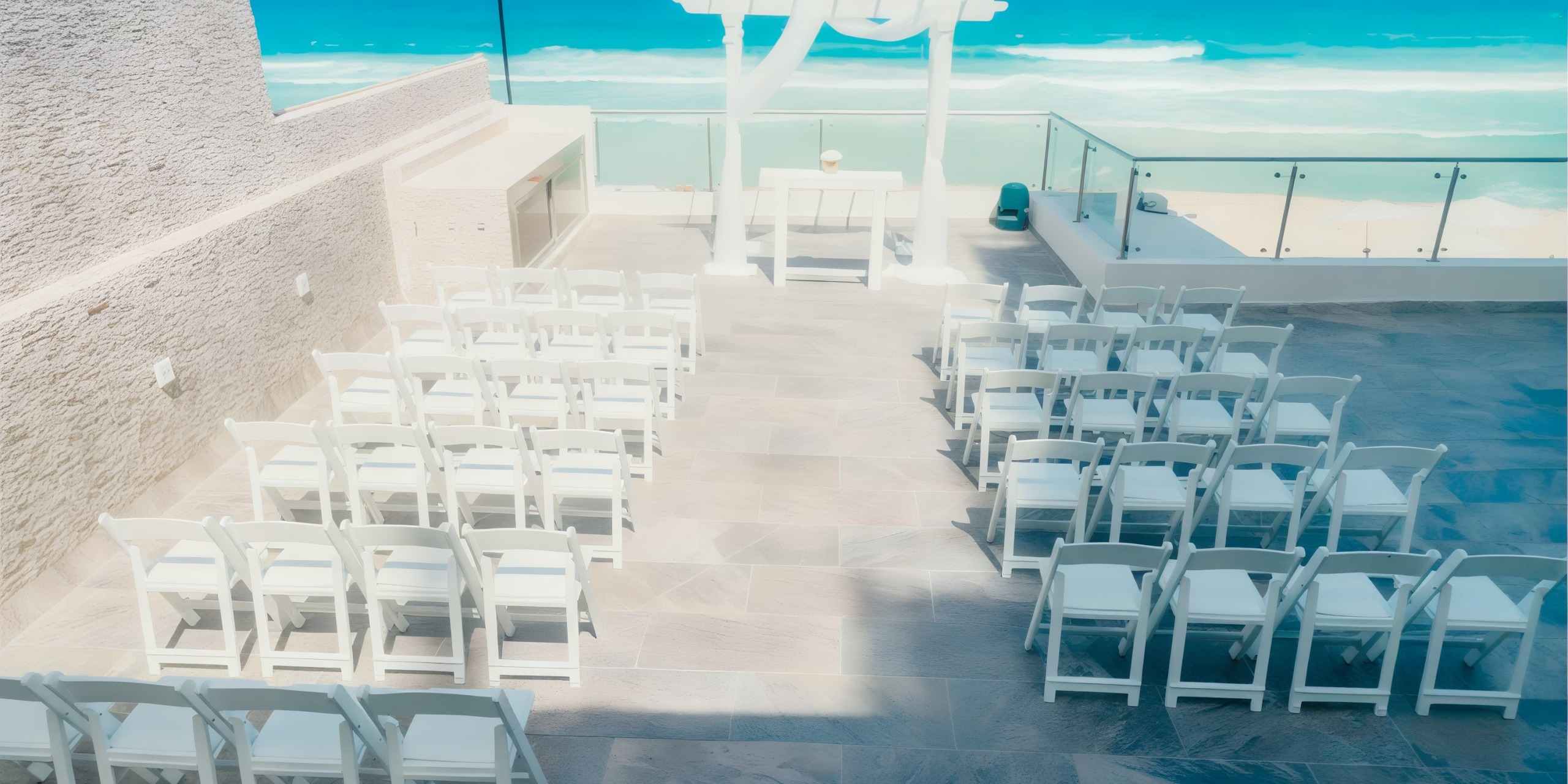 A stunning outdoor wedding setup at Hard Rock Cancun, featuring rows of white chairs facing a beautifully adorned wedding arch, all overlooking the breathtaking ocean on a sunny day.
