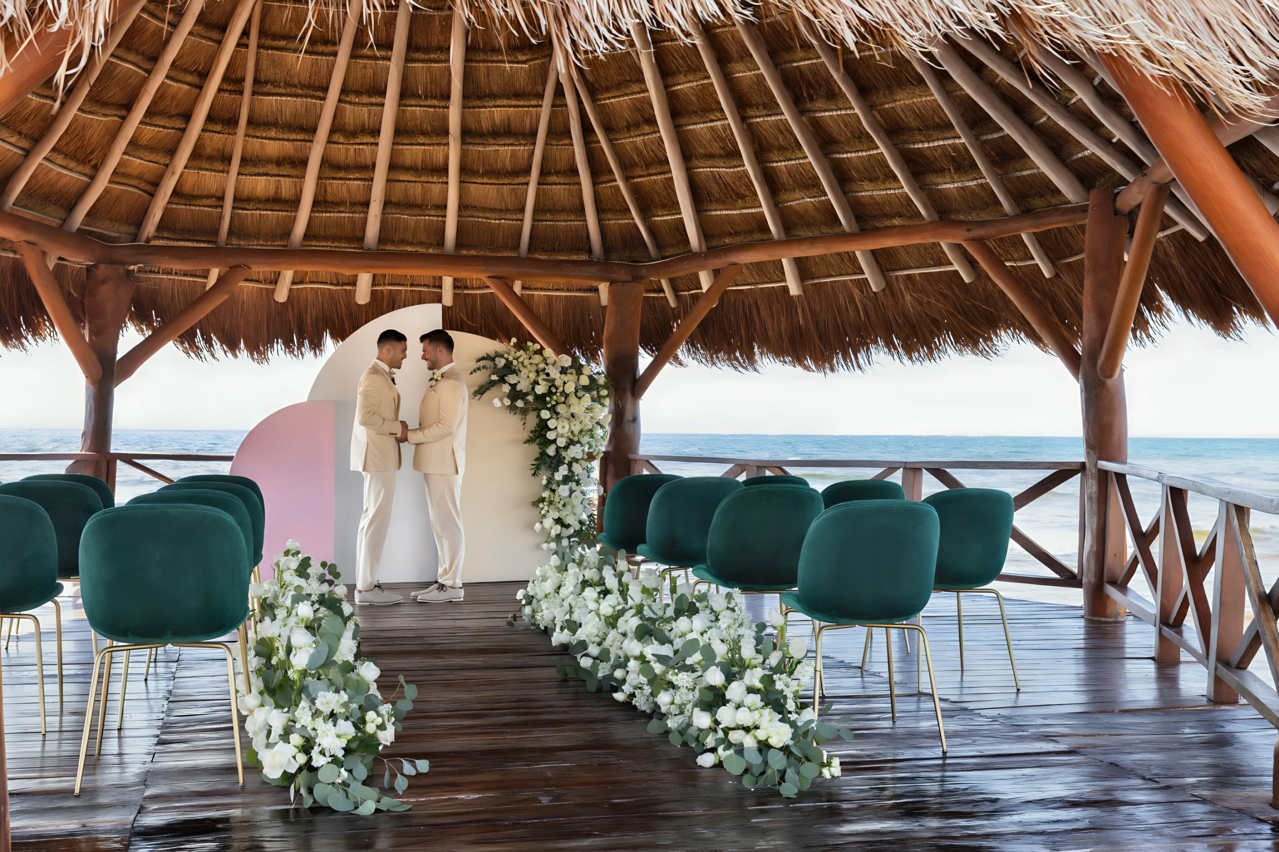 Same sex grooms getting married gay men LGBTQ+ wedding under a palapa thatched roof gazebo near the ocean at Hyatt Ziva Riviera Cancun enjoying the luxury wedding package