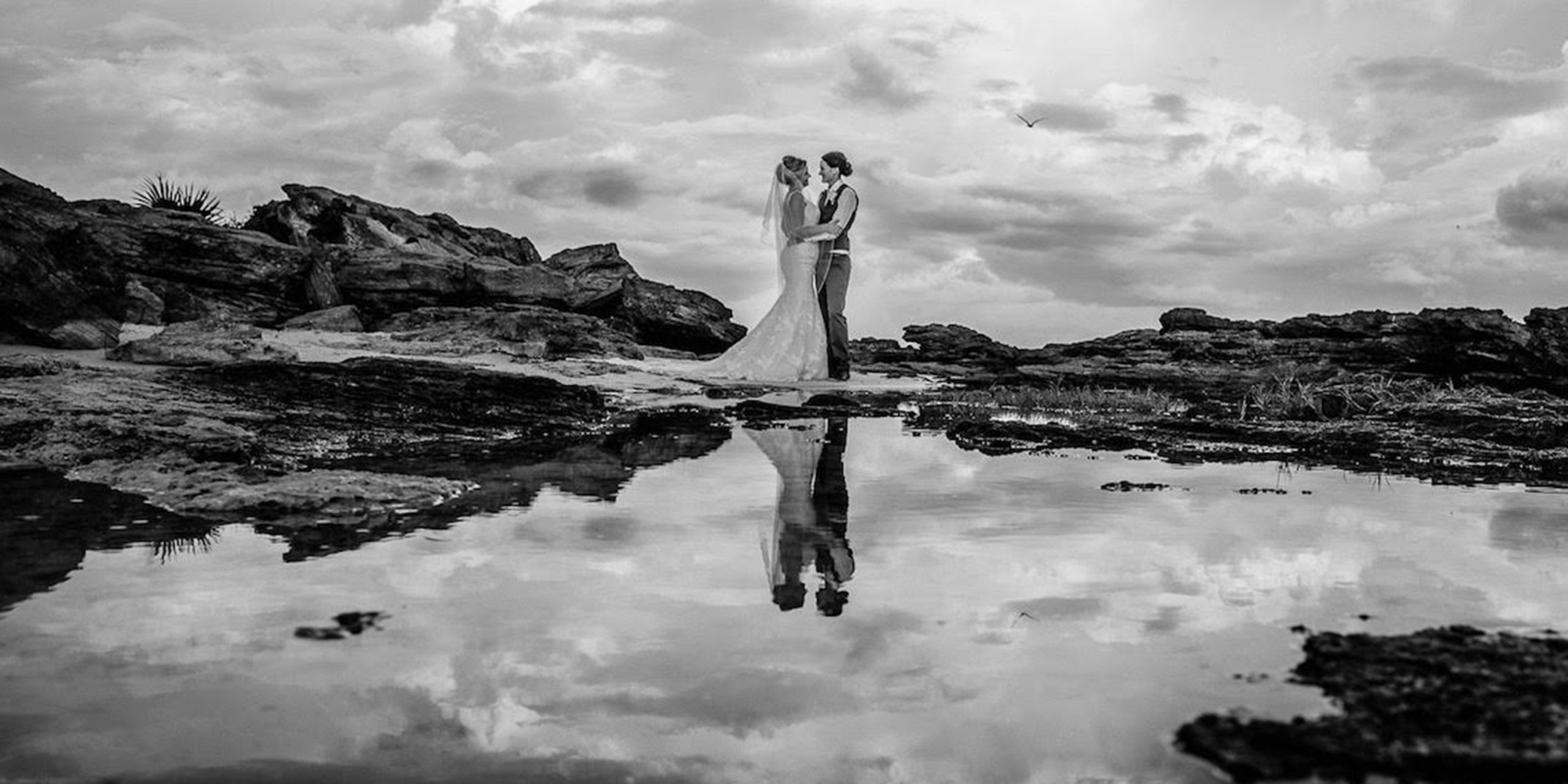 Tiana and Jessica post on the rocky beach at their dream destination wedding by Destify