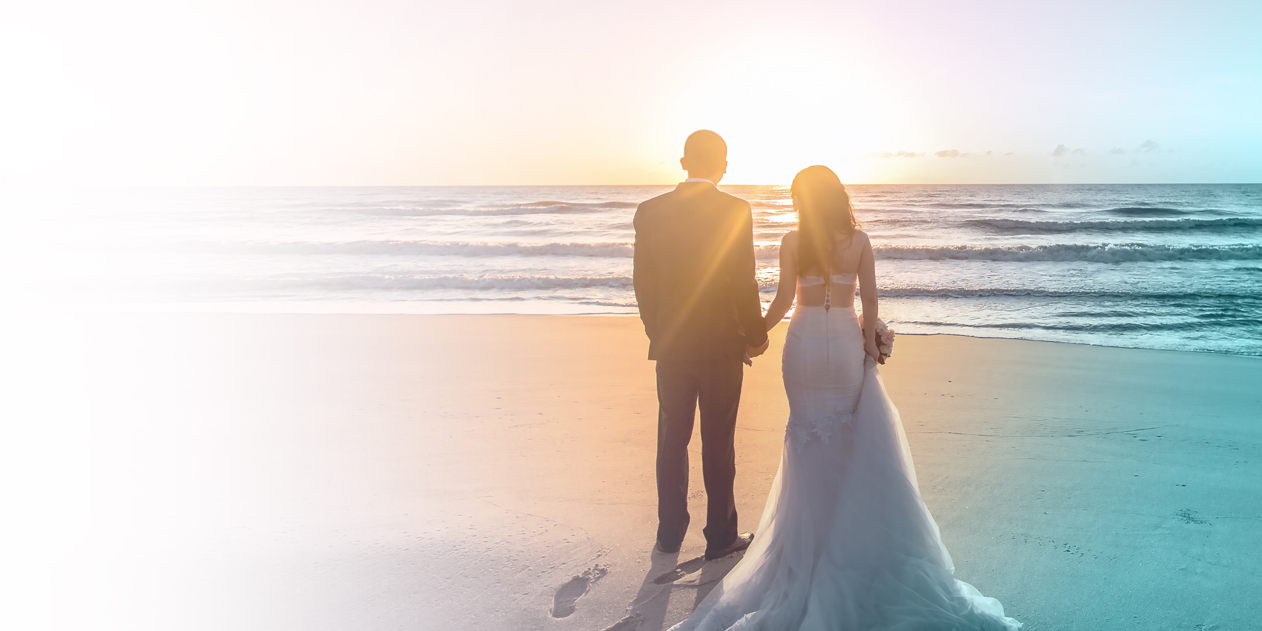 Newly married bride and groom husband and wife standing on the beach together during a sunset