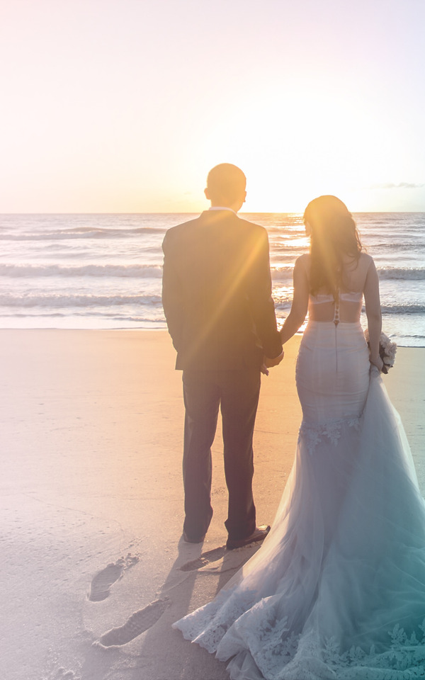 Newly married bride and groom husband and wife standing on the beach together during a sunset