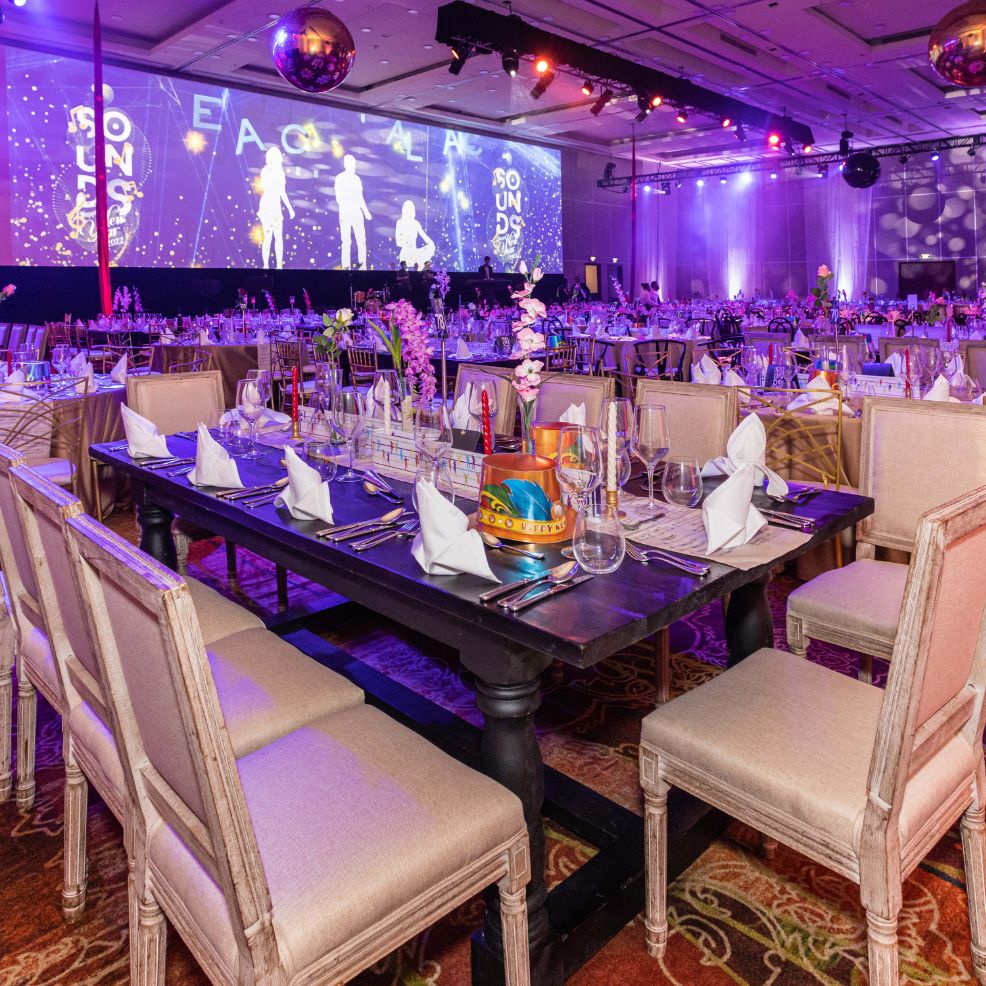 Elegant banquet hall with decorated tables and a stage setup for a destination wedding, lit in purple.