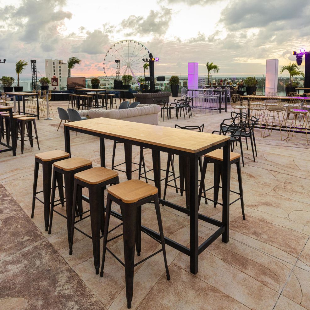 Outdoor patio set for a destination wedding, with wooden tables, stools, Ferris wheel and ocean views.