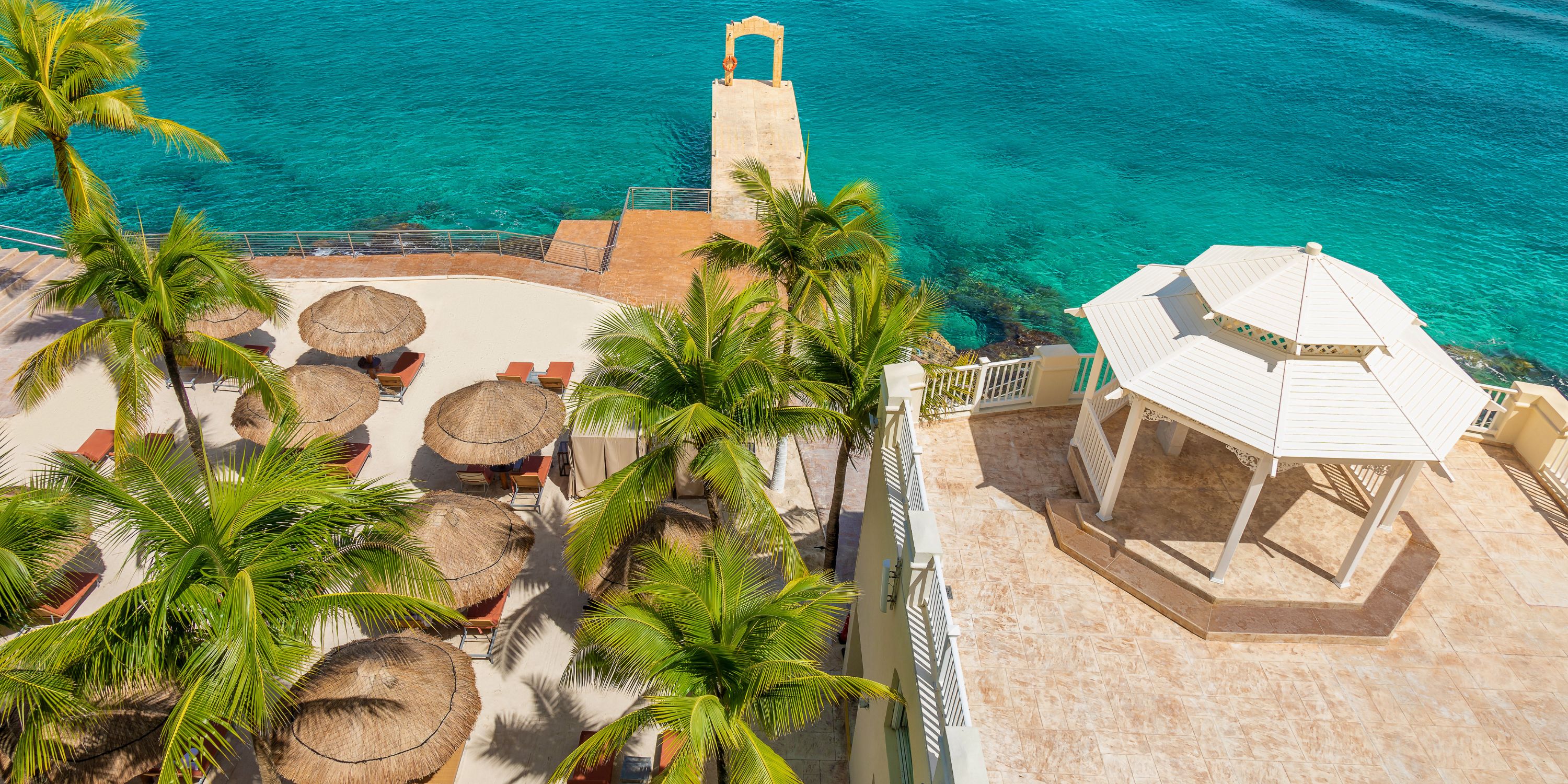 Aerial view of Cozumel Palace, ideal for a destination wedding, with palapas, palms, and a pier over blue water.
