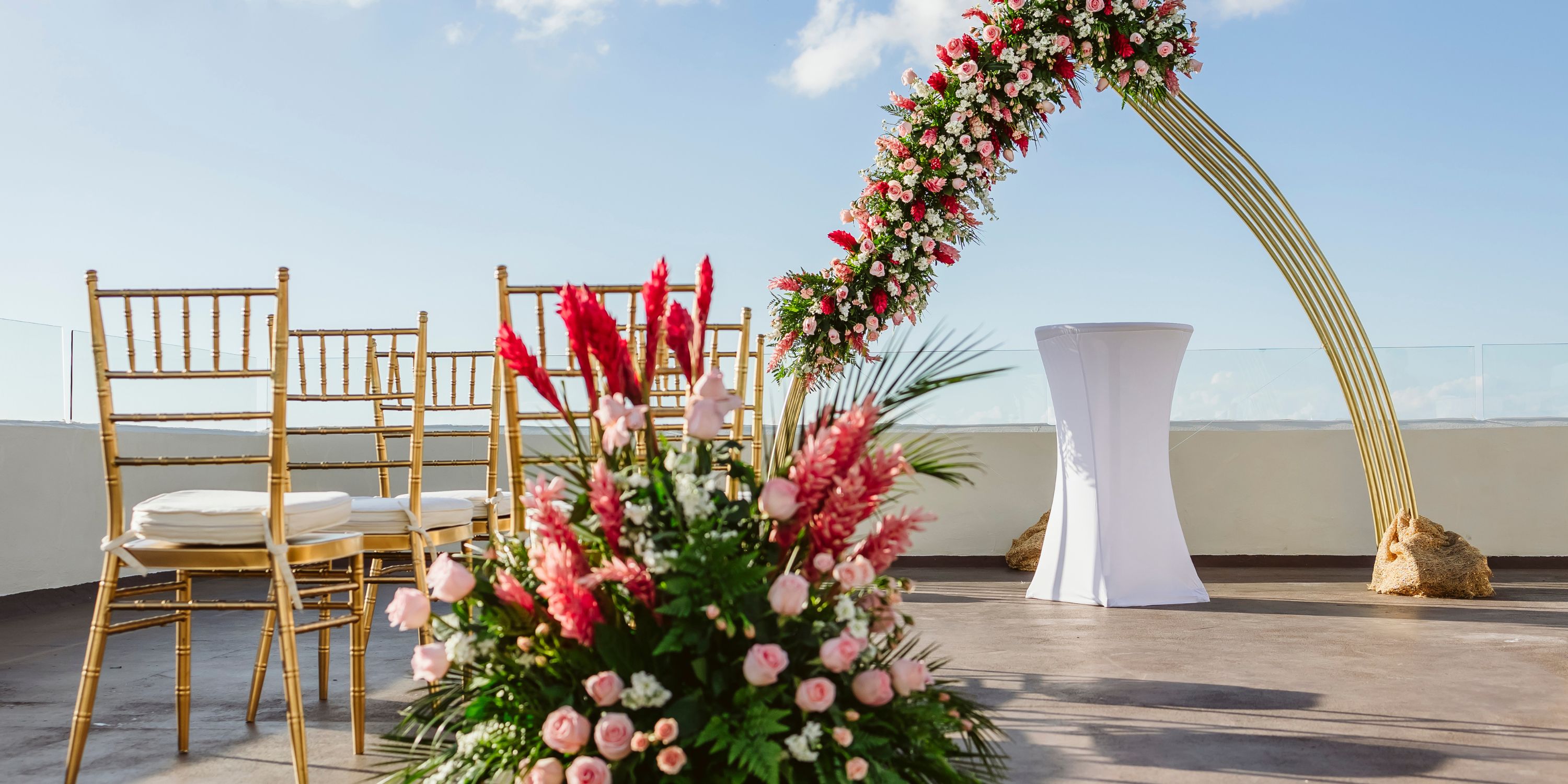 Destination wedding at Cozumel Palace featuring gold chairs and a floral arch beneath a clear blue sky.