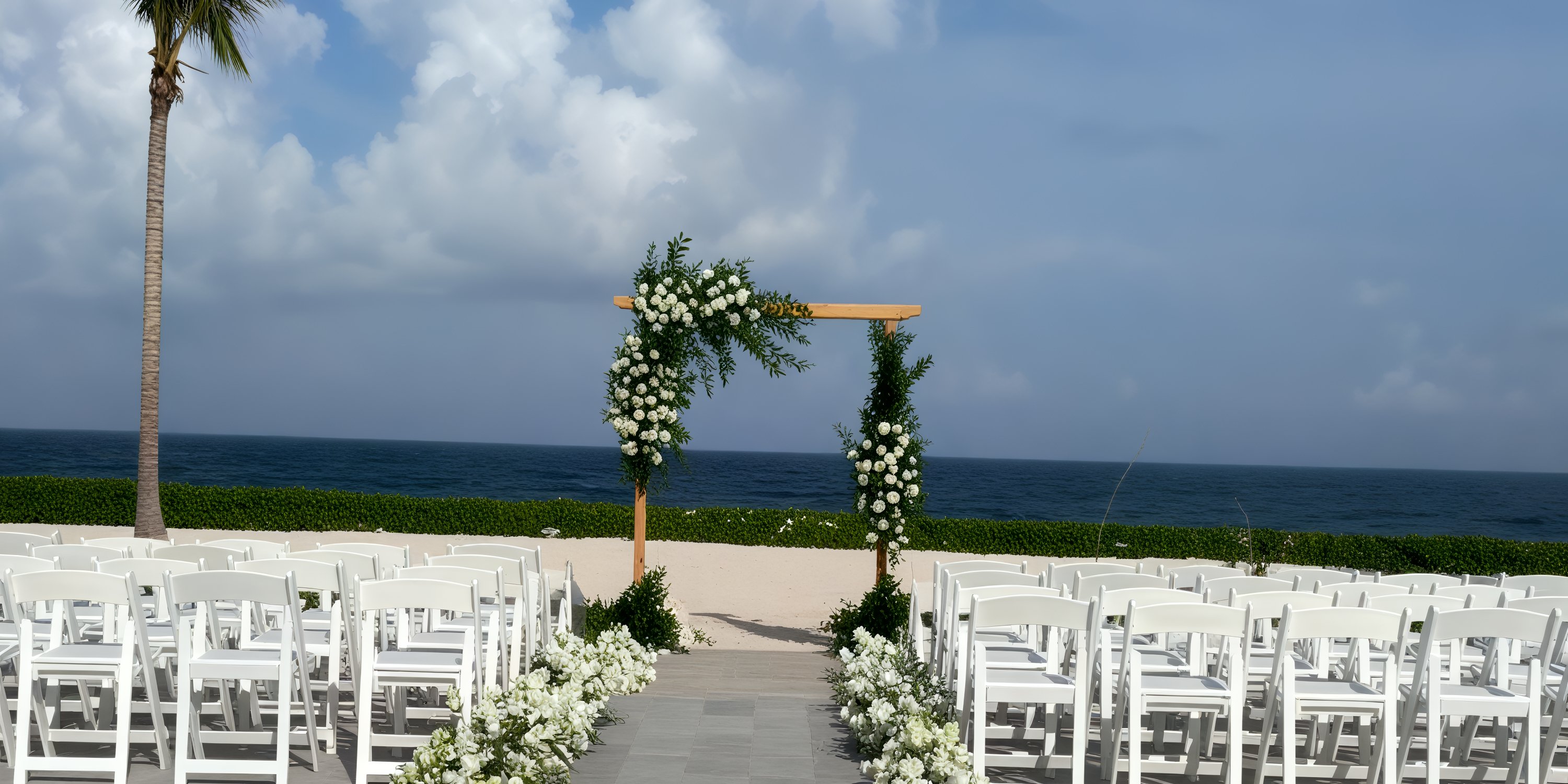 A picturesque destination wedding setup featuring white chairs and a floral arch, perfectly oriented towards the ocean.