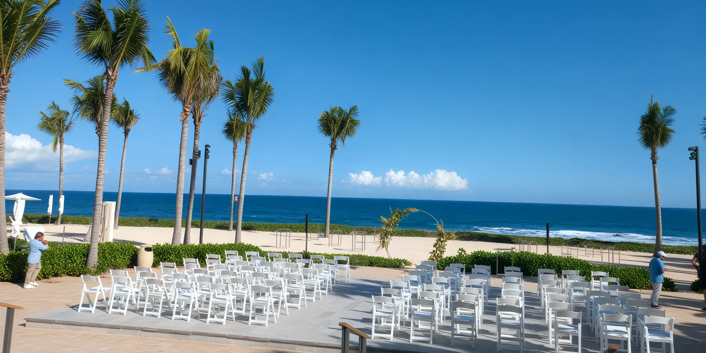 A beautiful destination wedding setup features rows of white chairs arranged by the beach, all under a clear blue sky.