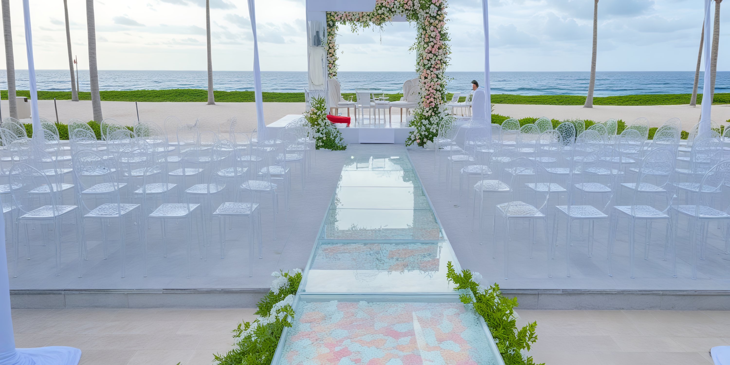 A picturesque destination wedding setup on the beachfront, featuring a clear aisle lined with white chairs all facing the ocean.