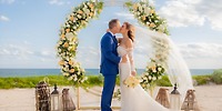 Bride and groom share a kiss beneath a floral arch at their destination wedding on the Hilton Tulum beach.