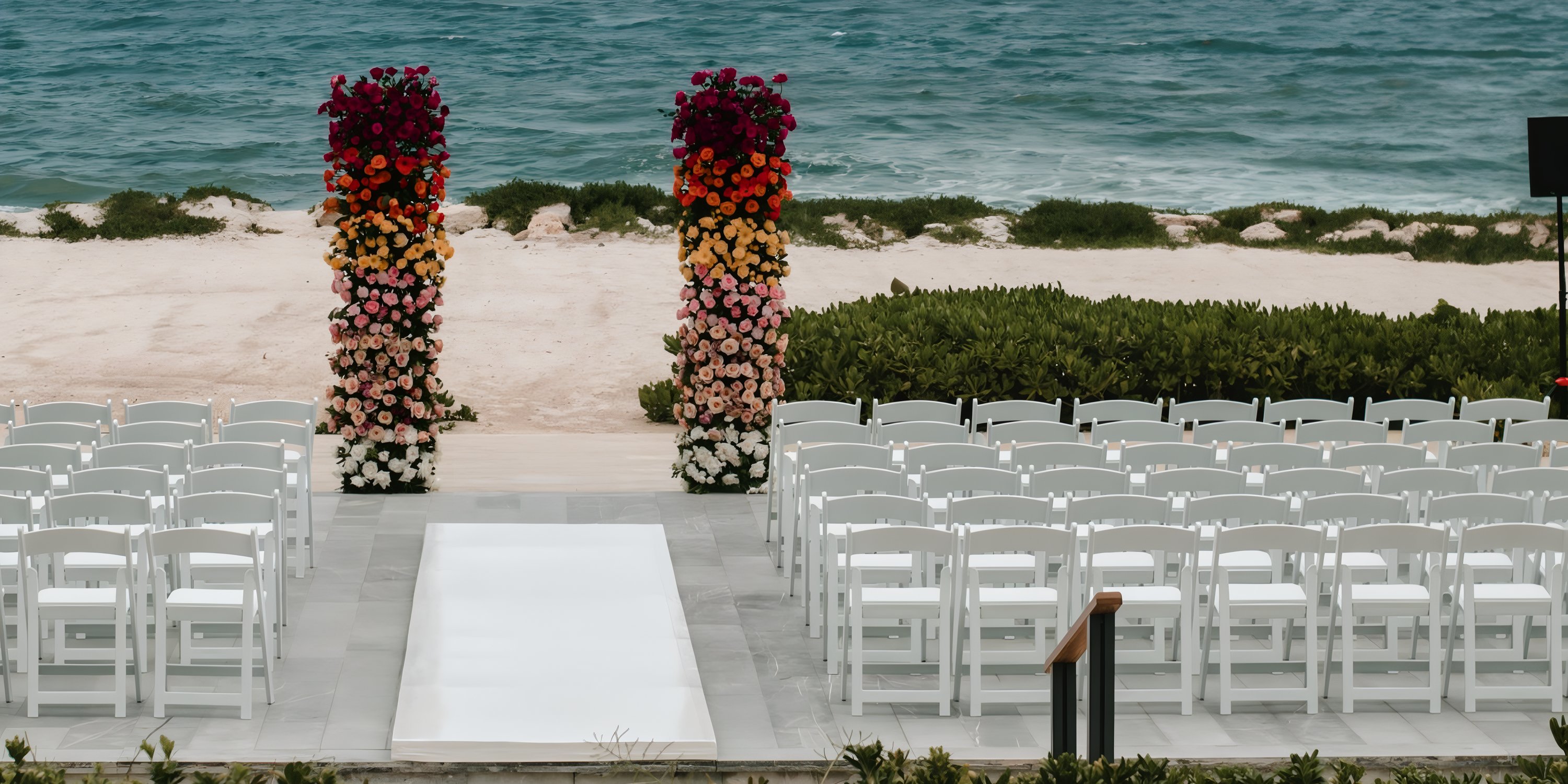 White wedding chairs look toward floral pillars by the beach at a destination wedding in Hilton Tulum.