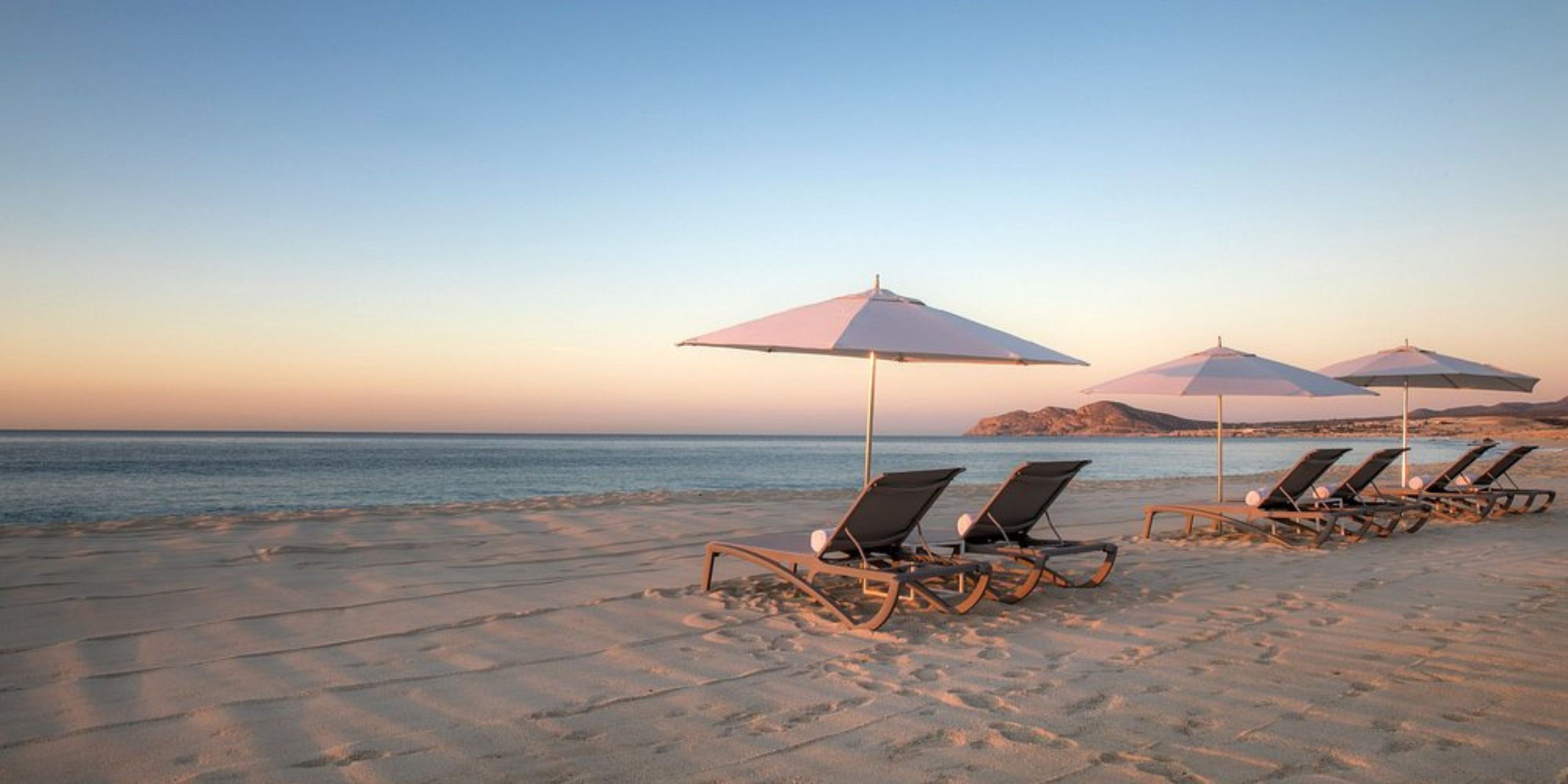 Lounge chairs with umbrellas on the beach at Le Blanc Spa Resort Los Cabos, a destination wedding spot at sunset.