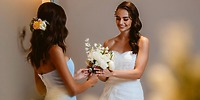 Two women smile at each other, holding white flowers at a destination wedding at Le Blanc Spa Resort.