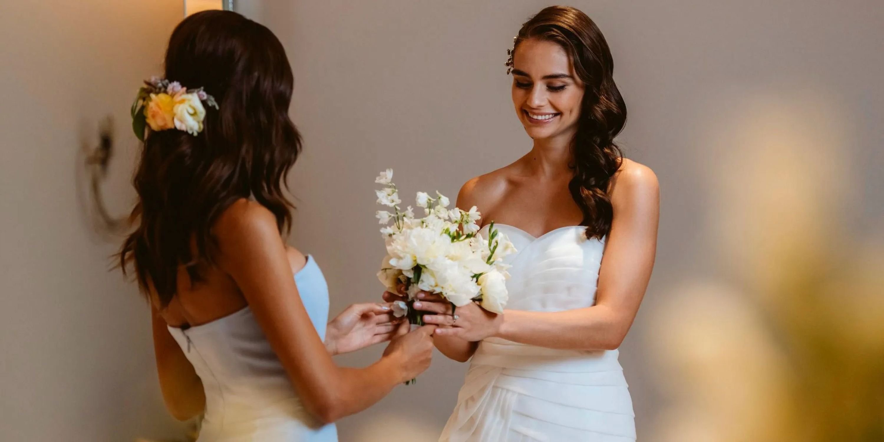 Two women smile at each other, holding white flowers at a destination wedding at Le Blanc Spa Resort.