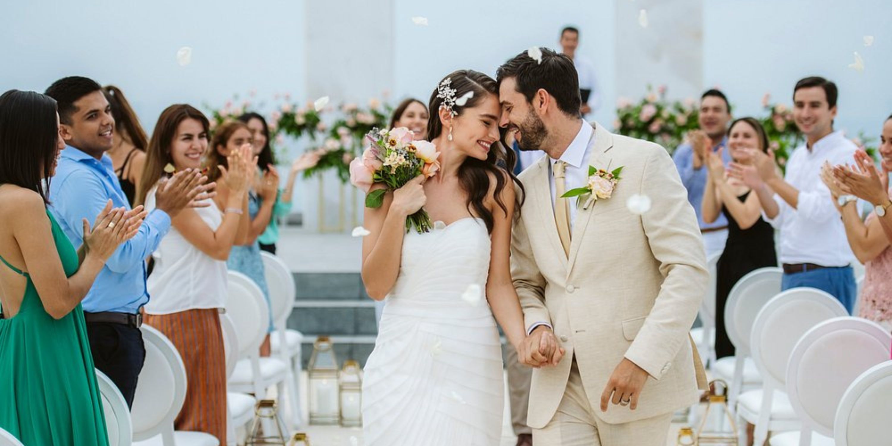 The wedding couple walks the aisle at a destination wedding as guests cheer and toss flower petals.