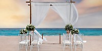 Stunning destination wedding setup at Le Blanc Spa Resort All Inclusive Adults Only, featuring elegant white chairs and a beautiful floral arch.