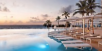 The infinity pool at Le Blanc Spa Resort, surrounded by swaying palm trees and overlooking the ocean at sunset, offers a breathtaking backdrop for a destination wedding.