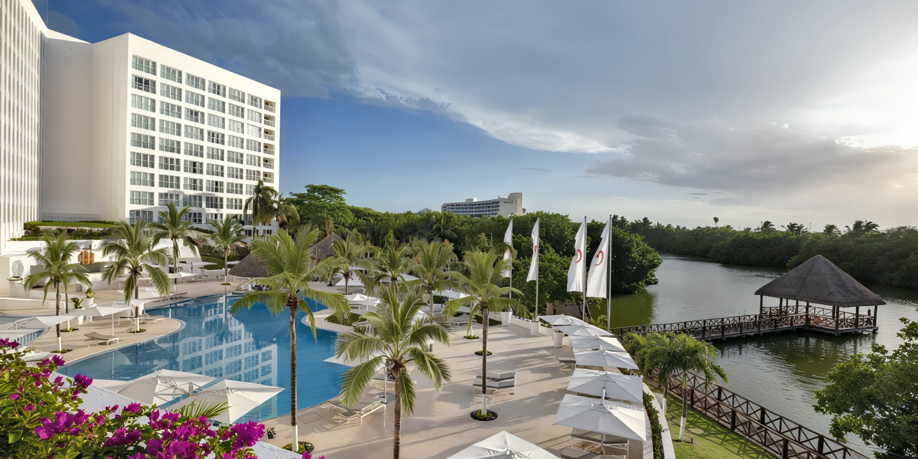 Le Blanc Spa Resort offers an idyllic setting for a destination wedding, featuring a spacious adults-only pool surrounded by swaying palm trees, lush greenery, relaxing lounge chairs, and tranquil river views.