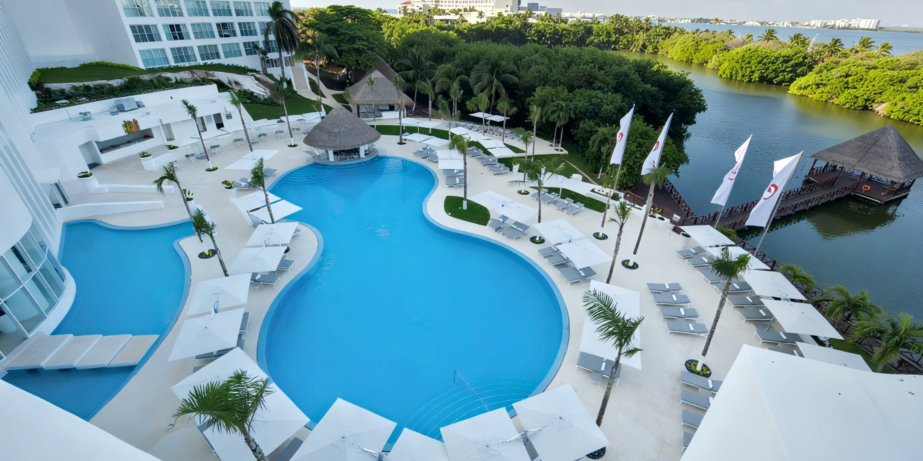 A stunning aerial view of Le Blanc Spa Resort’s pool area showcases elegant lounge chairs, umbrellas, and a sparkling lagoon—a picturesque setting perfect for a destination wedding.