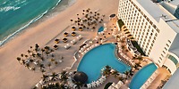 Aerial view of Le Blanc Spa Resort, an adults-only destination wedding venue, featuring a stunning pool surrounded by palm trees and elegant lounge chairs.