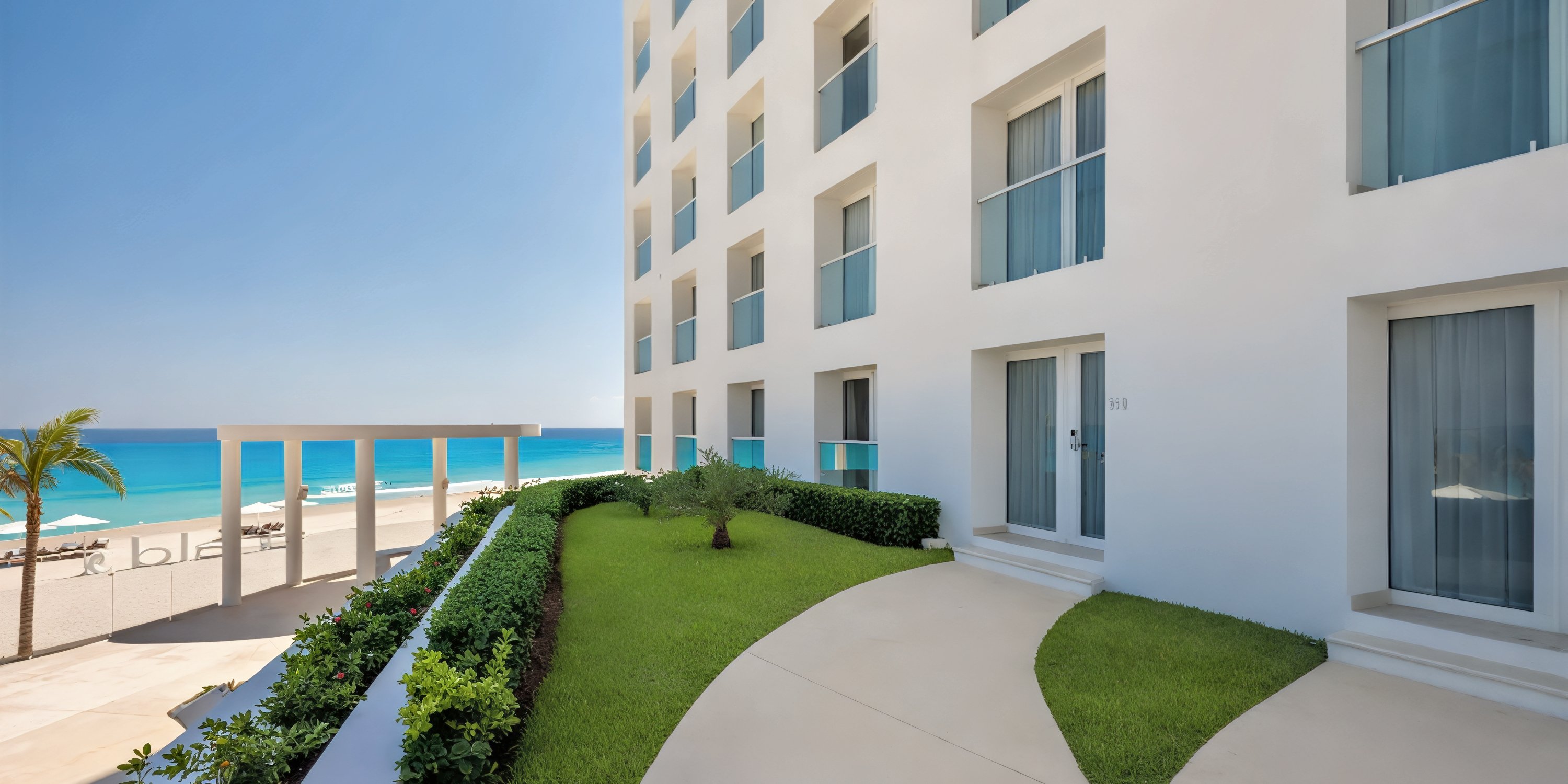 Le Blanc Spa Resort: A modern beachfront venue with sweeping ocean views, expansive windows, and a lush green lawn—perfect for a dream destination wedding under the blue sky.