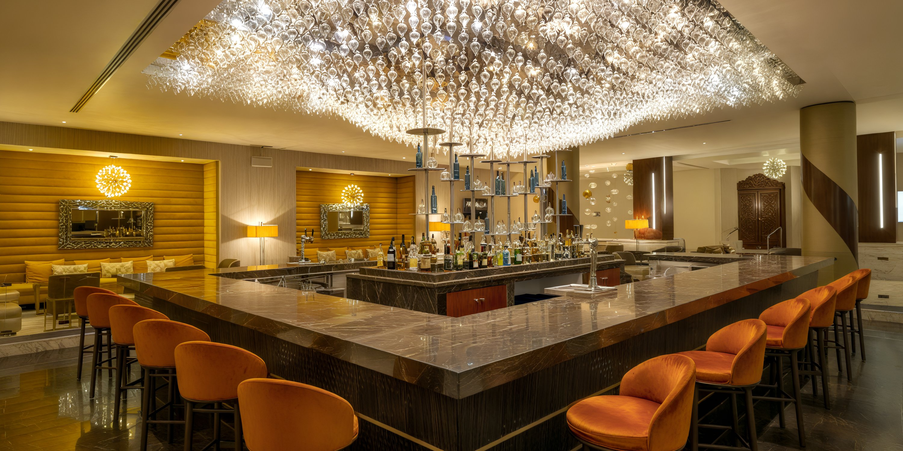 Moon Palace Cancun: An elegant U-shaped bar featuring vibrant orange chairs and a stunning glass chandelier, perfect for hosting an unforgettable destination wedding.
