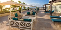 Moon Palace Cancun's rooftop patio is the perfect setting for a destination wedding, featuring lounge furniture, umbrellas, and palms set against a clear sky.
