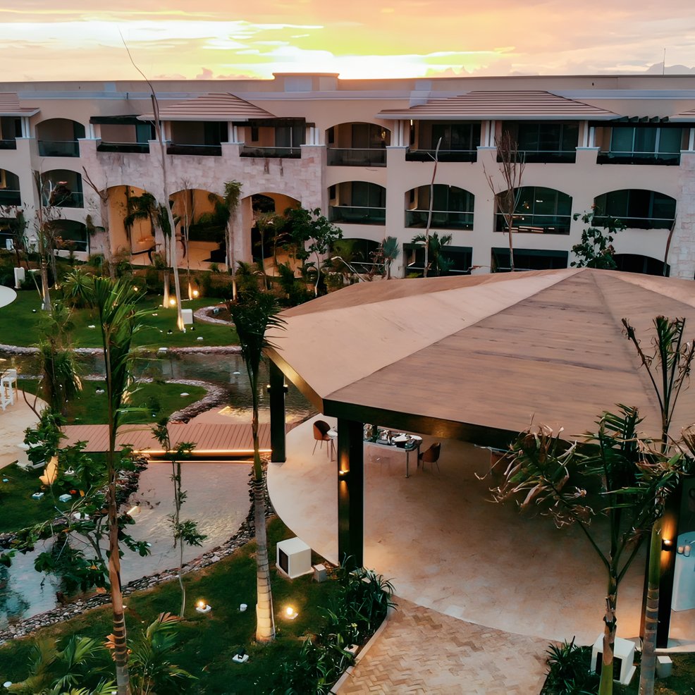 A modern hotel courtyard at sunset, ideal for a destination wedding, with gardens, gazebo, and lit paths.