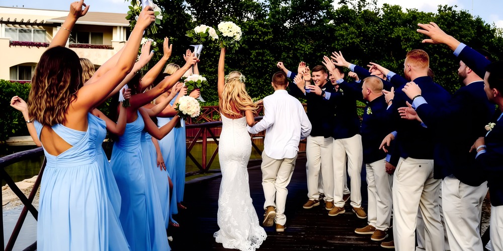 At Moon Palace The Grand, the bride and groom make their way across a wooden bridge, surrounded by cheers and applause at their beautiful destination wedding.