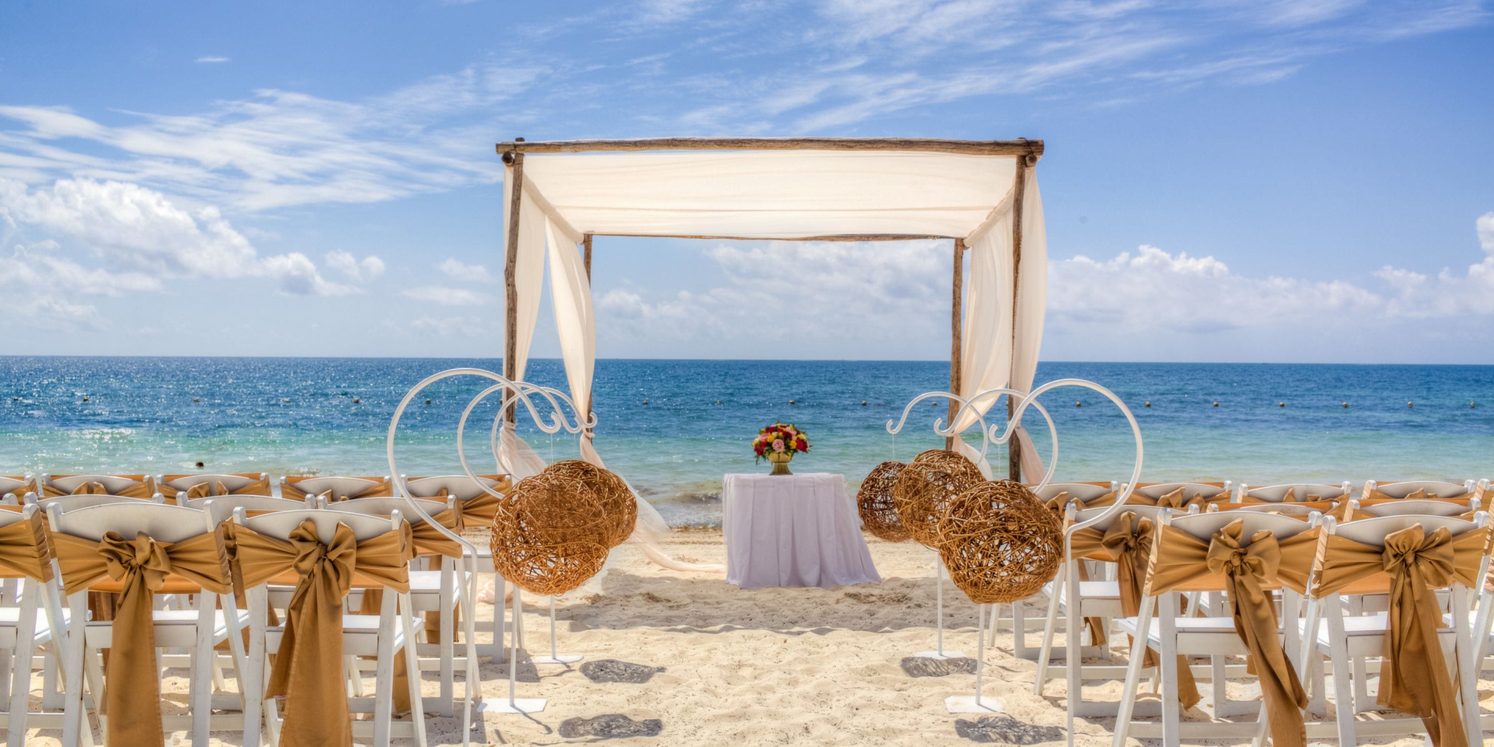 Ocean Coral and Turquesa destination wedding setup with chairs, arch, and table beneath a canopy.