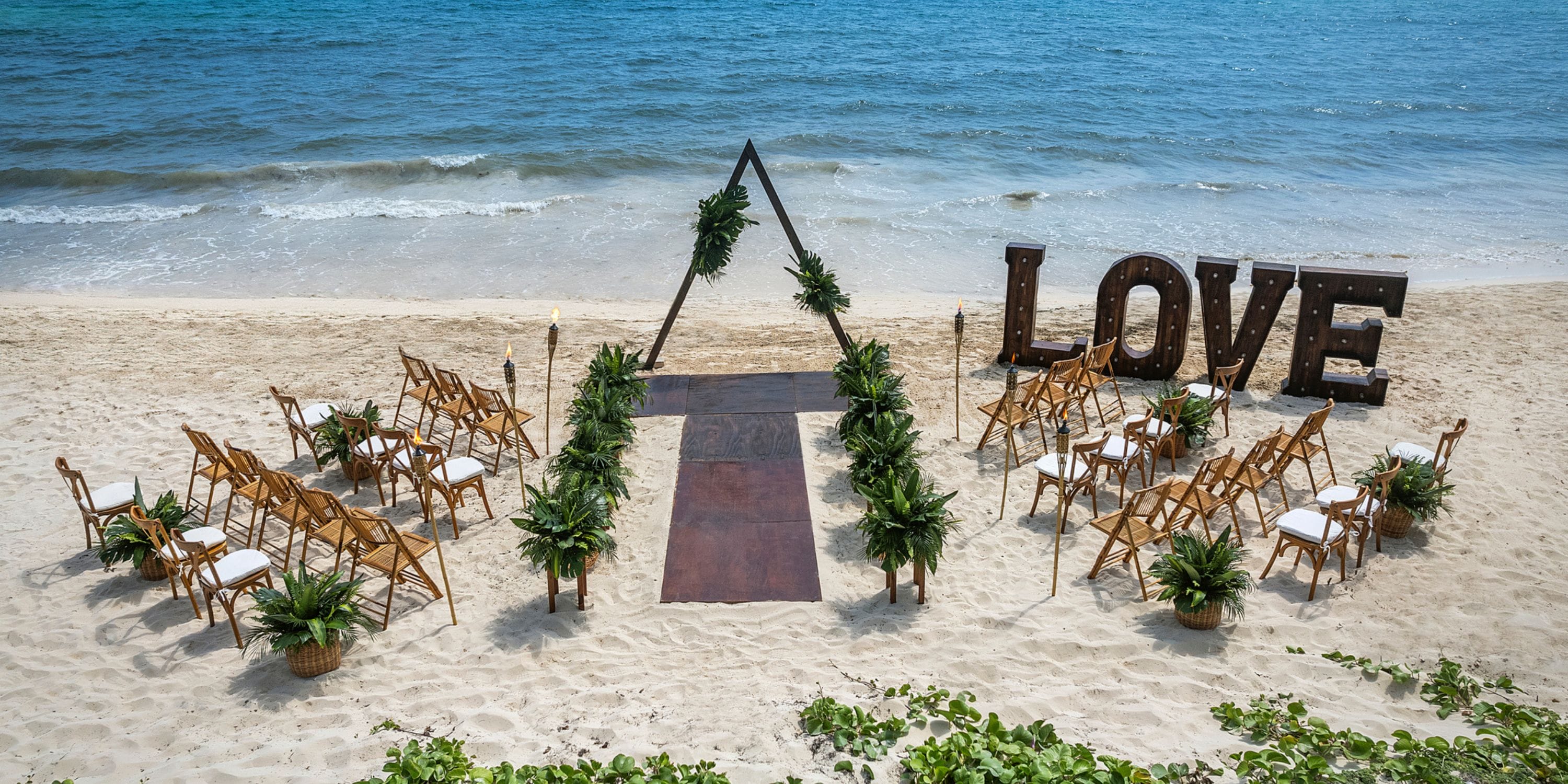 Destination wedding at Ocean Coral and Turquesa with chairs, lush greenery, and large "LOVE" letters on beach.