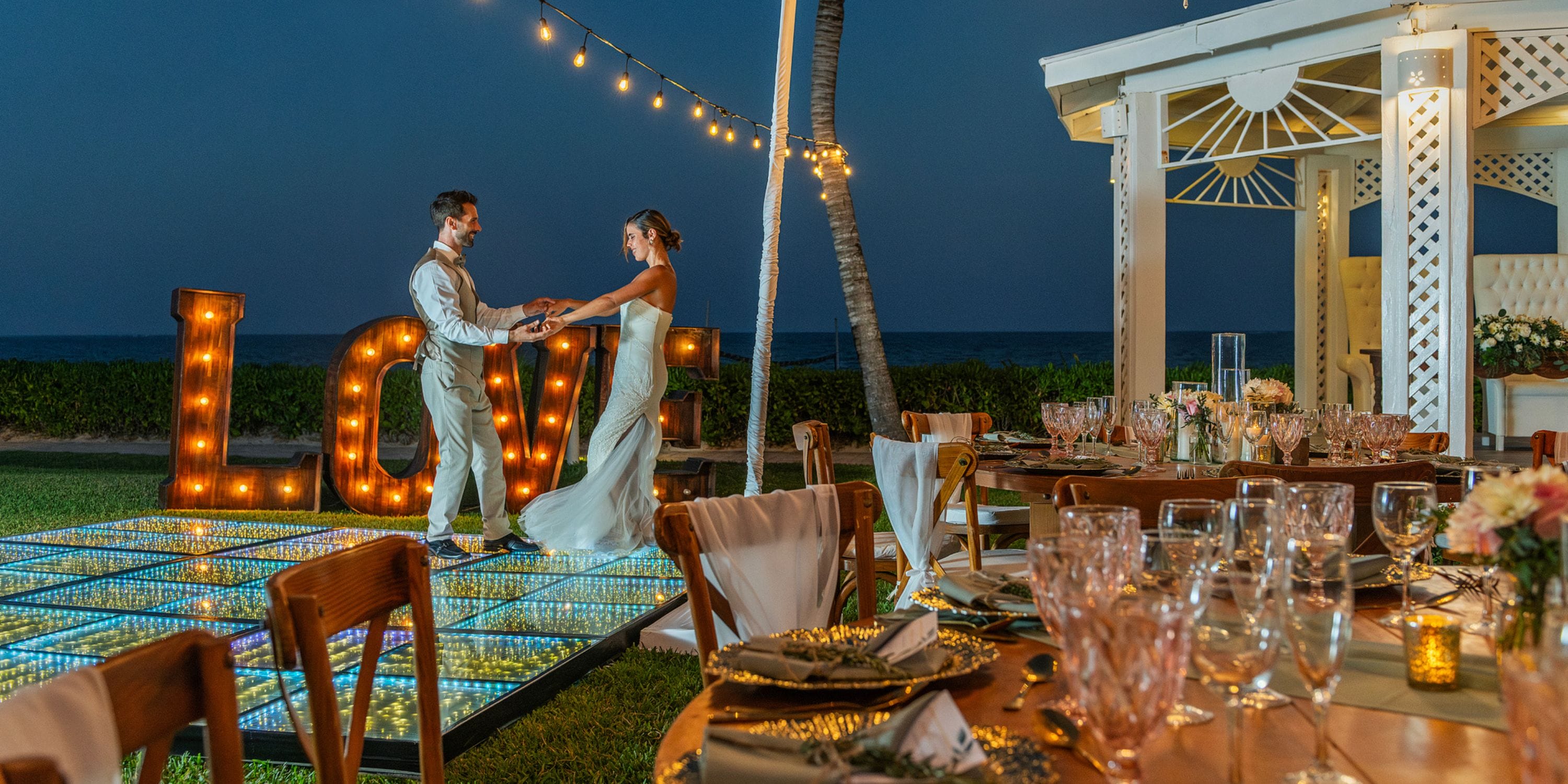 Bride and groom share a wedding dance on Ocean Coral and Turquesa's lit floor, "LOVE" lights outside.
