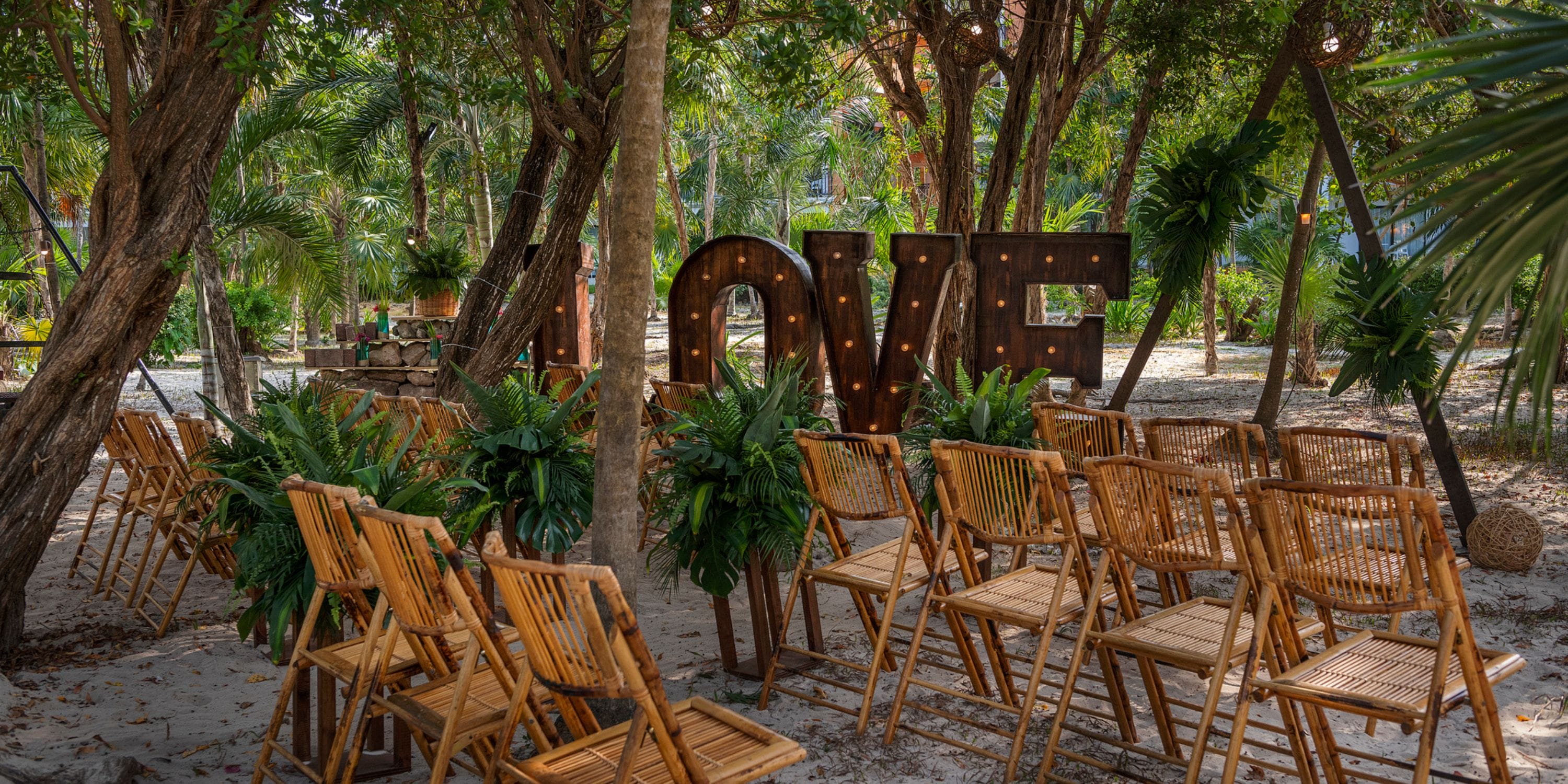Destination wedding at Ocean Coral and Turquesa with bamboo chairs and a big "LOVE" sign under the trees.