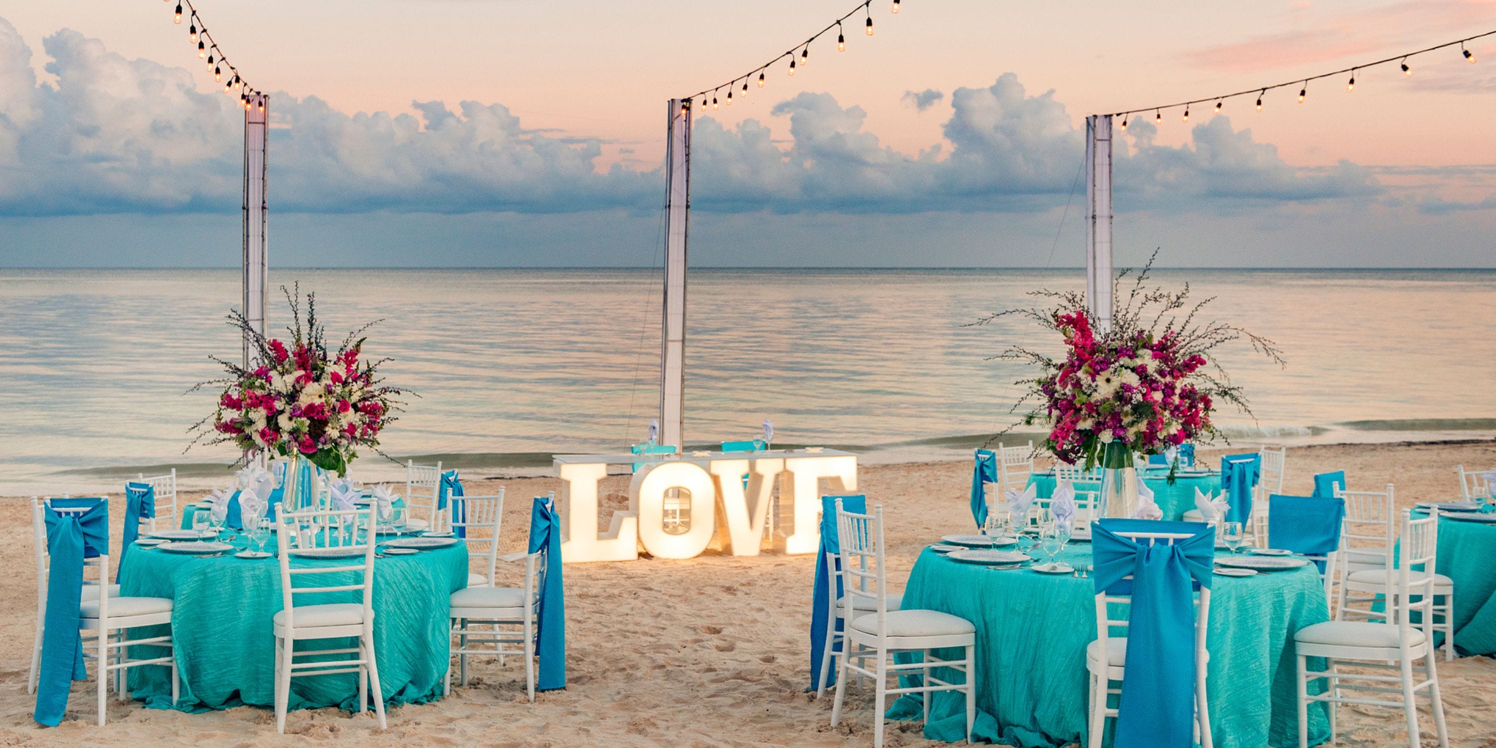 Destination wedding at Ocean Coral and Turquesa with turquoise tables, floral accents, and LOVE sign.
