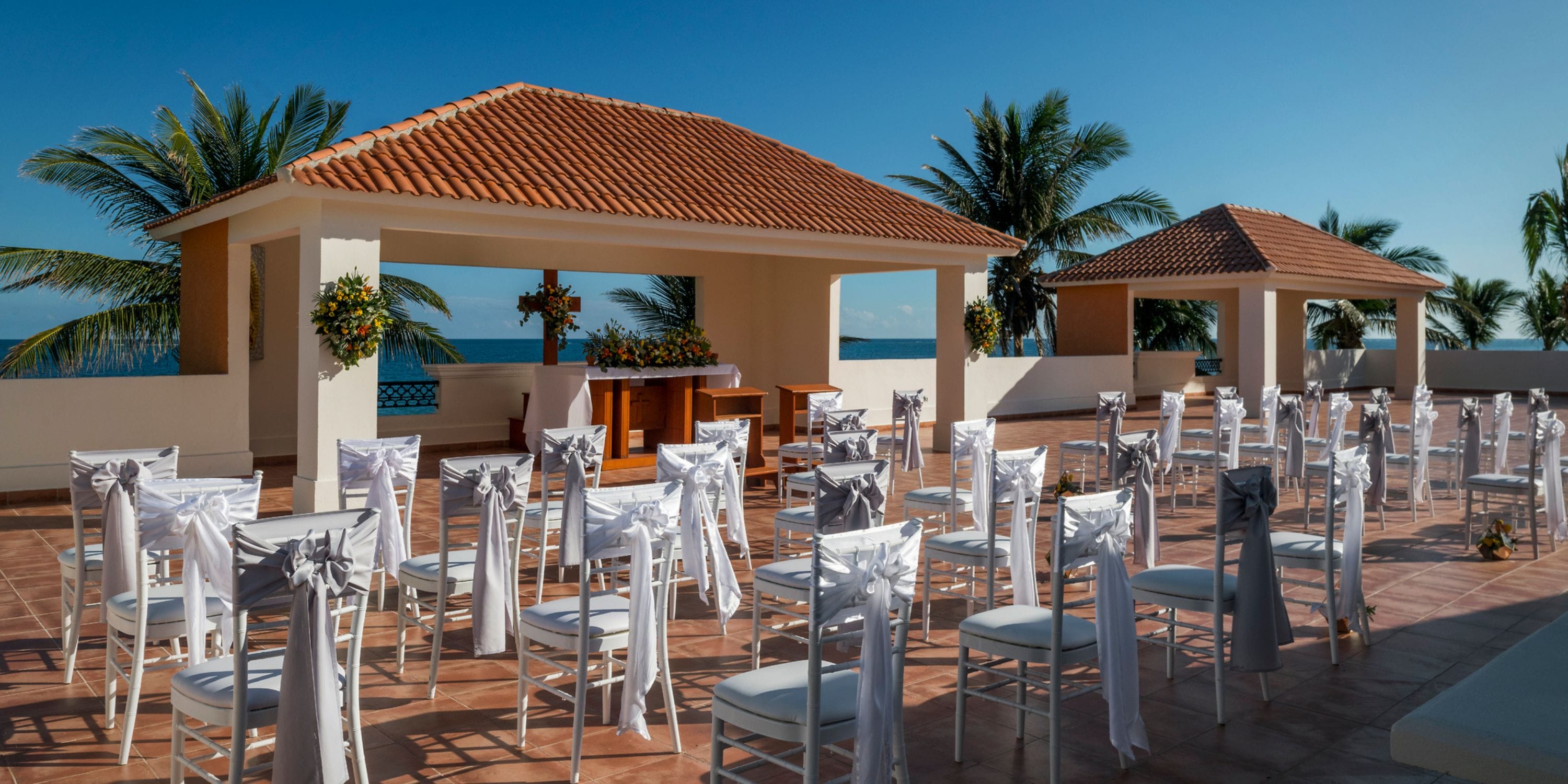 White chairs arranged in rows for a destination wedding ceremony beneath a bright, clear blue sky.