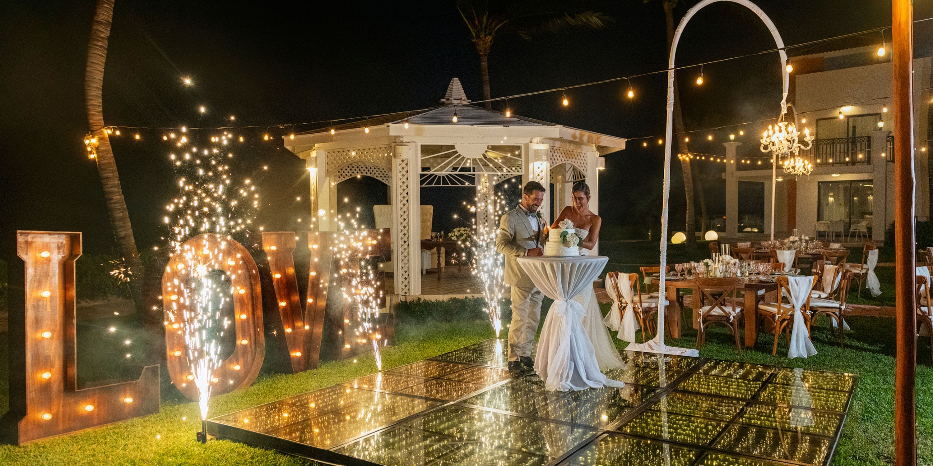 A couple cuts their wedding cake on a glowing dance floor at night during their destination wedding.