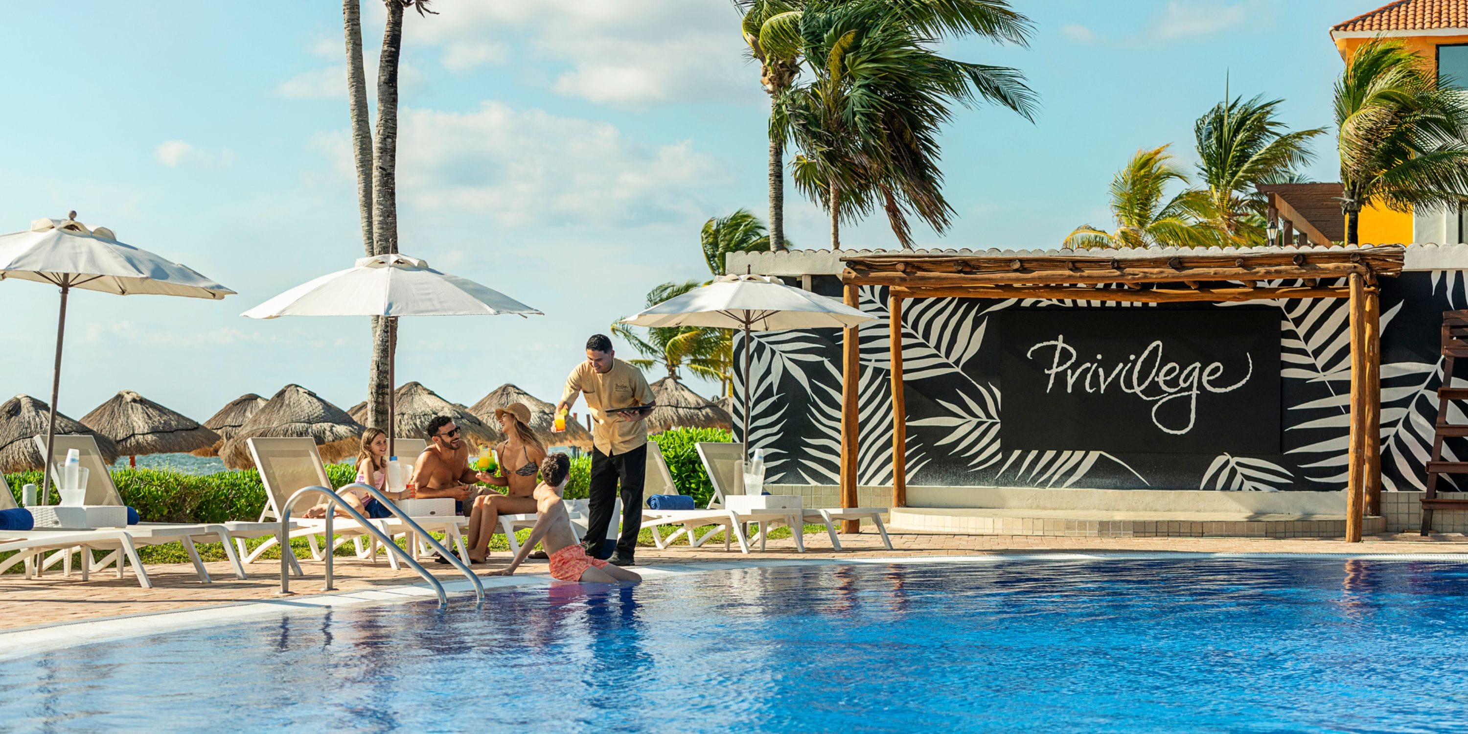 At Ocean Coral and Turquesa, a server brings drinks to wedding guests lounging by the pool.