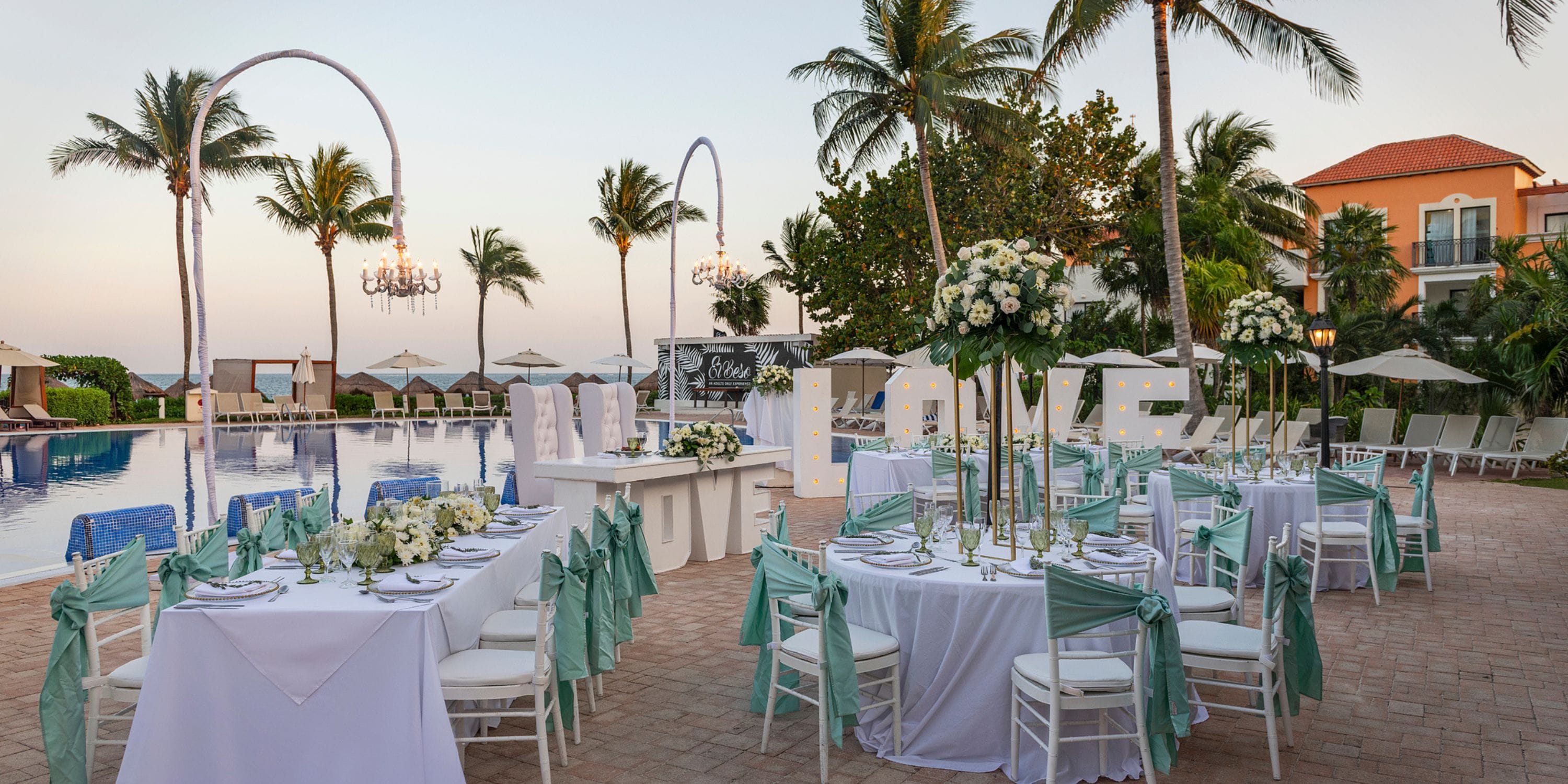 Destination wedding at Ocean Coral and Turquesa poolside with round tables, floral decor, and LOVE sign.